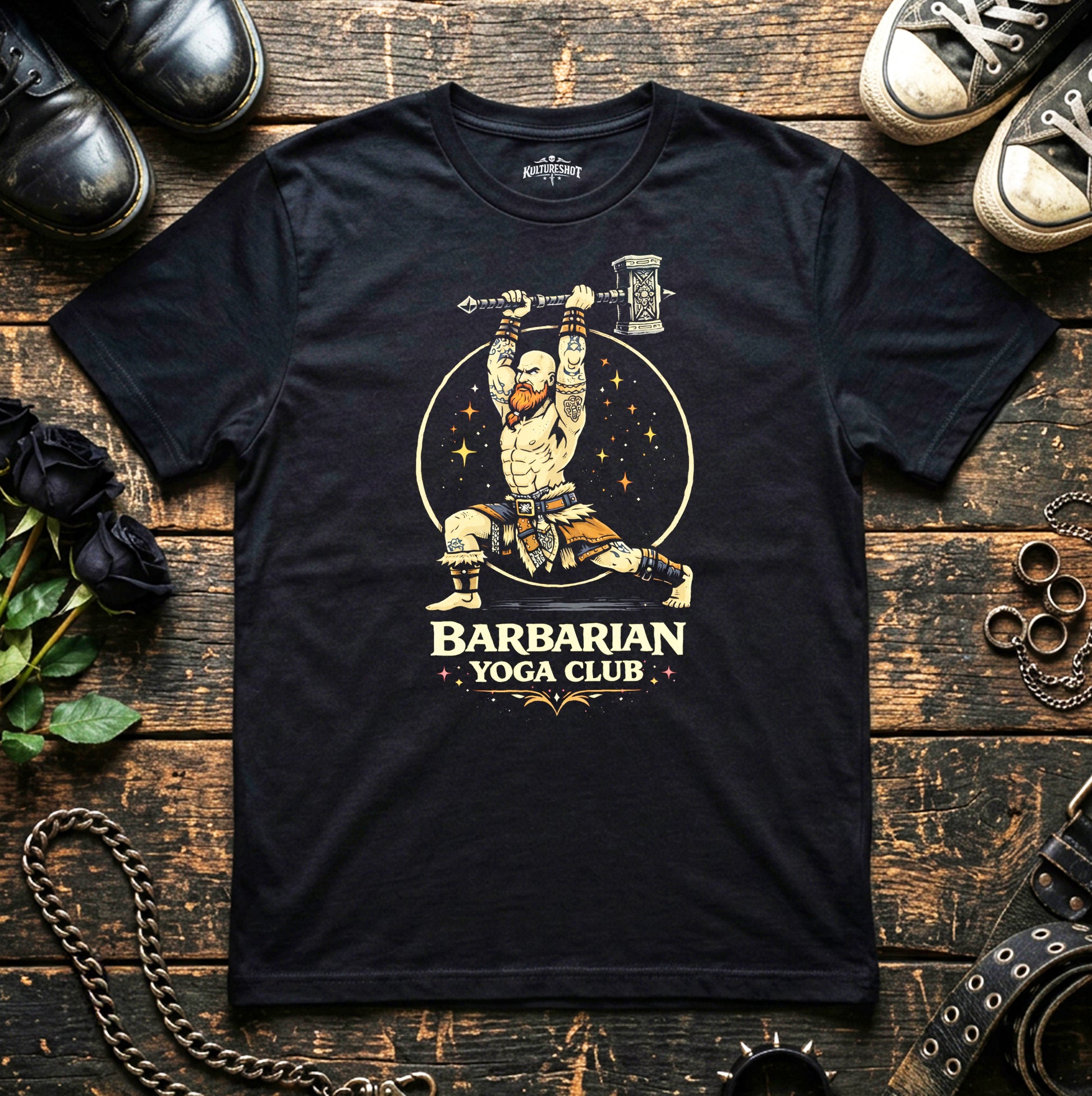 Black t-shirt with 'Barbarian Yoga Club' design on a wooden surface with shoes and decorative items.