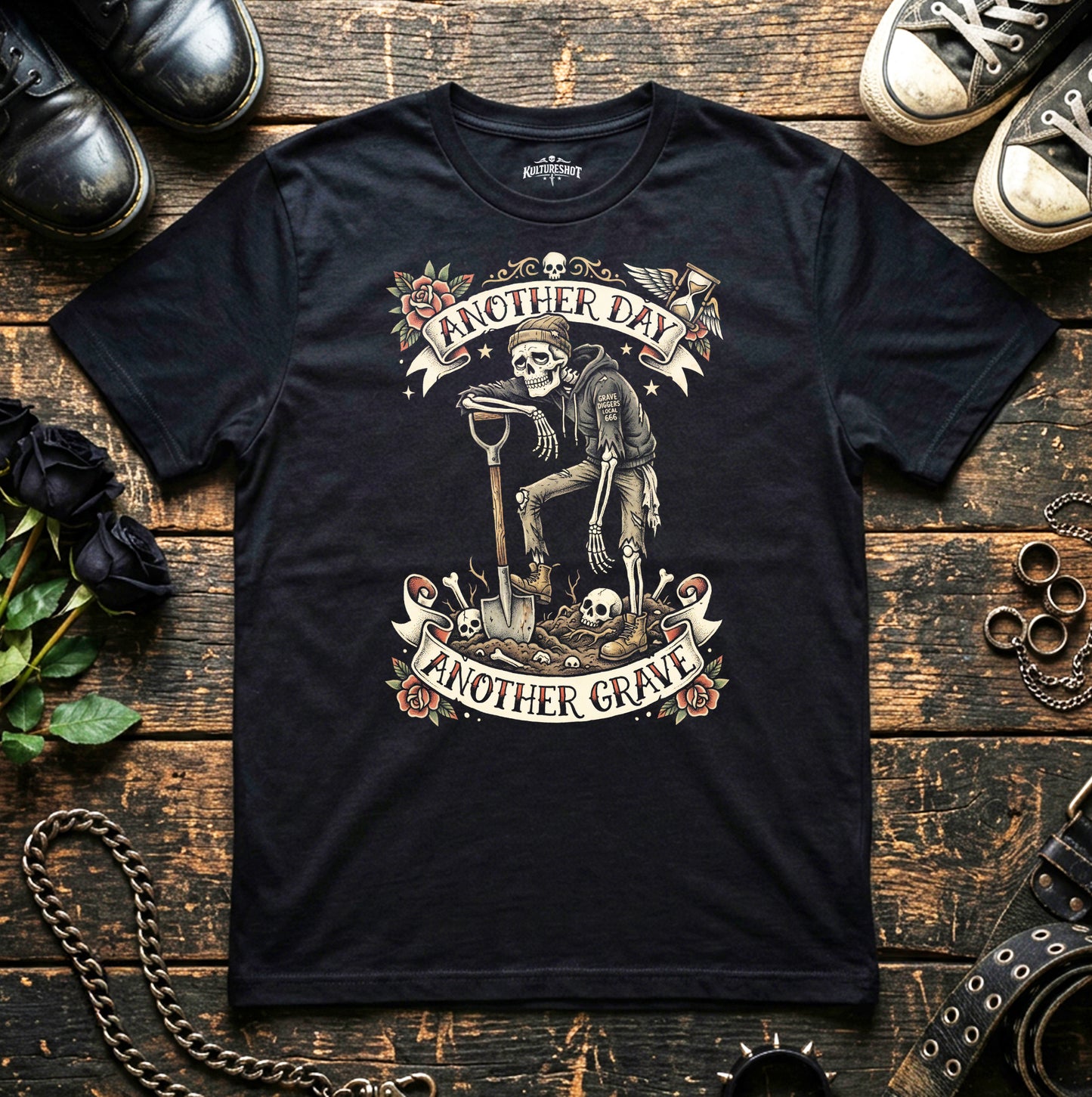 Black t-shirt with skeleton graphic and text 'Another Day, Another Grave' on a wooden surface with shoes and roses.