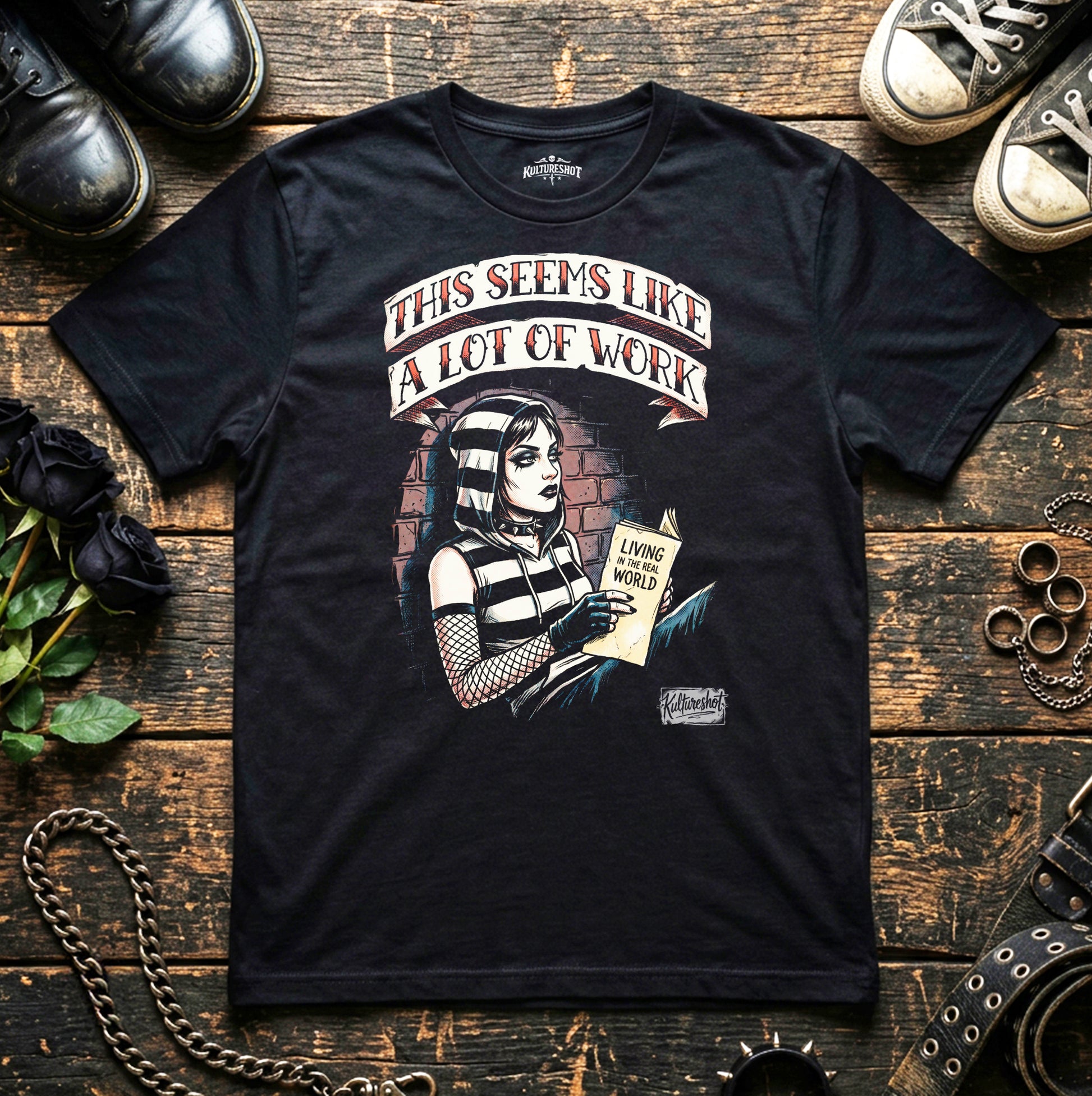 Black t-shirt with graphic design and text on a wooden surface with shoes and flowers.