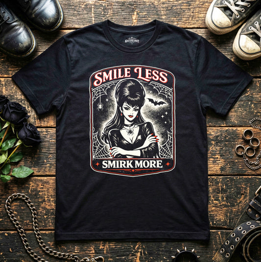 Black t-shirt with graphic design featuring a woman and text 'Smile Less, Smirk More' on a wooden surface.