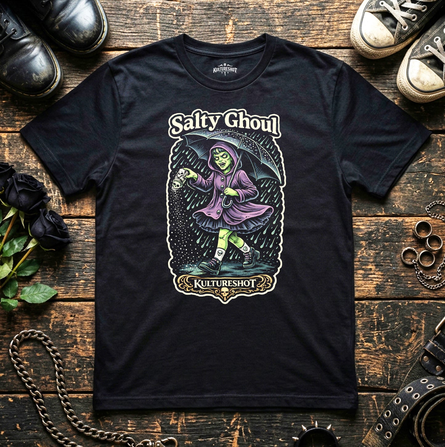 Black t-shirt with a graphic design of a character labeled 'Salty Ghoul' on a wooden surface with shoes and chains.