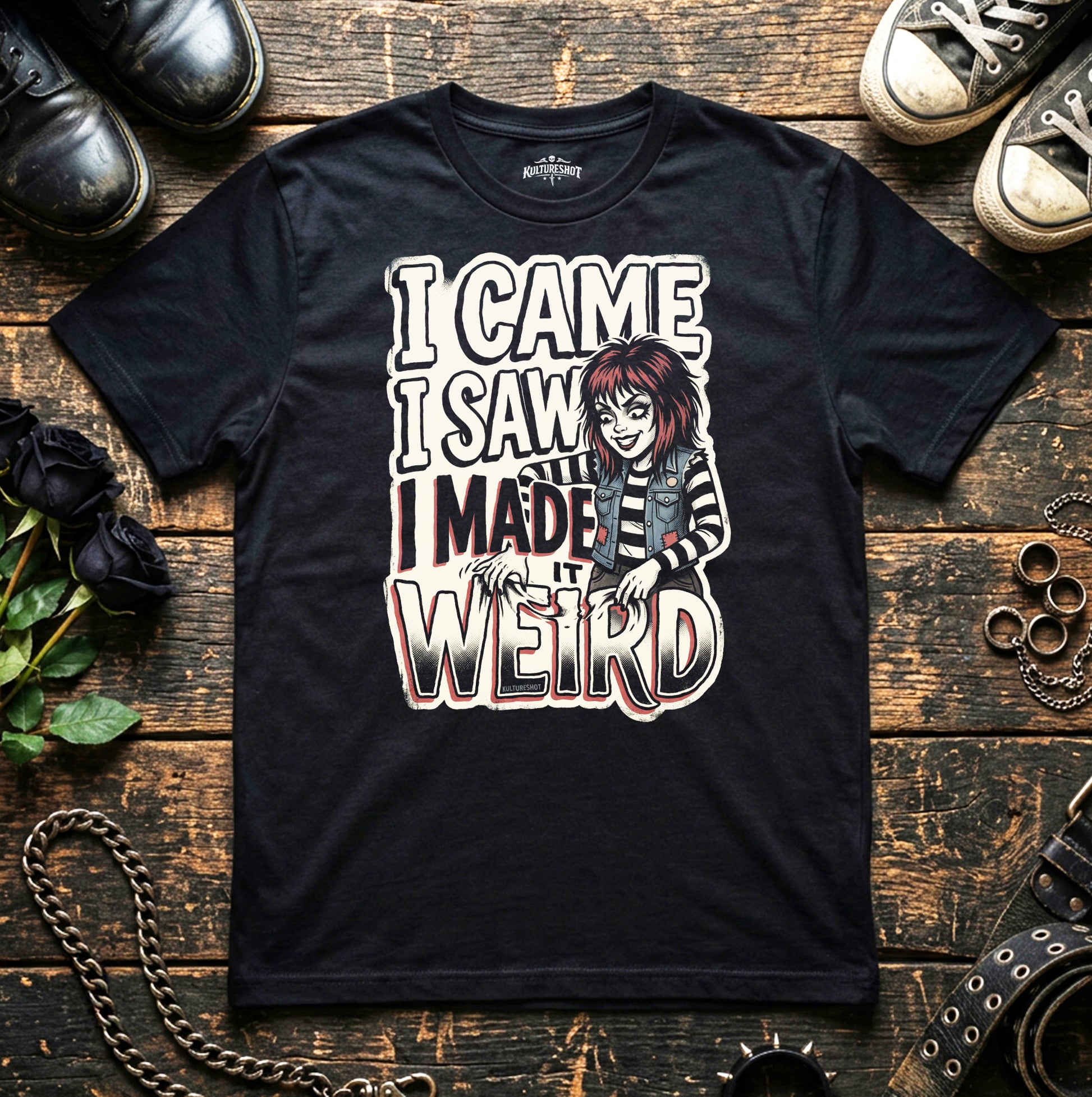 Black t-shirt with graphic design and text on a wooden surface with shoes and flowers.