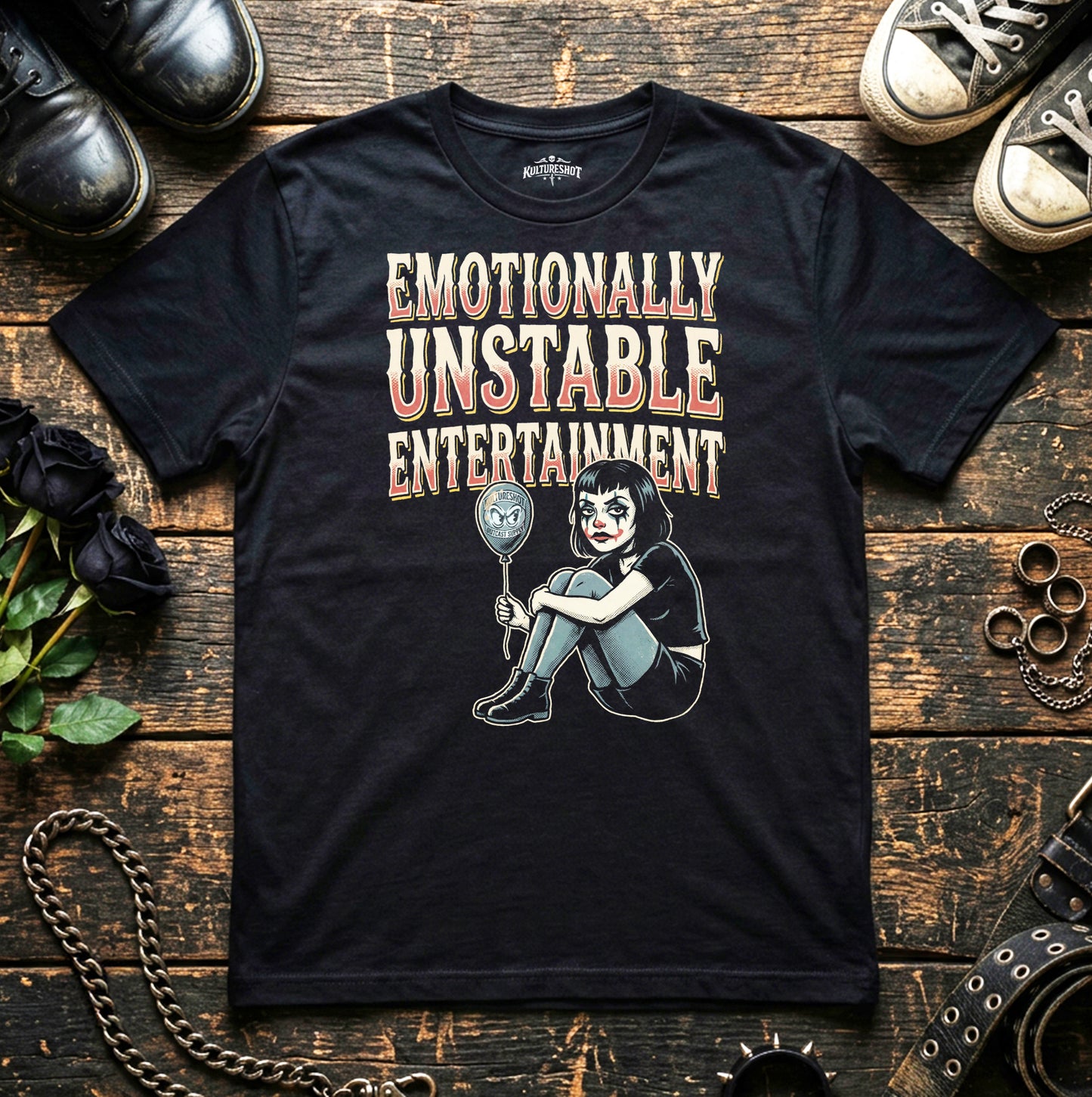 Black t-shirt with graphic design and text on a wooden surface with shoes and flowers.