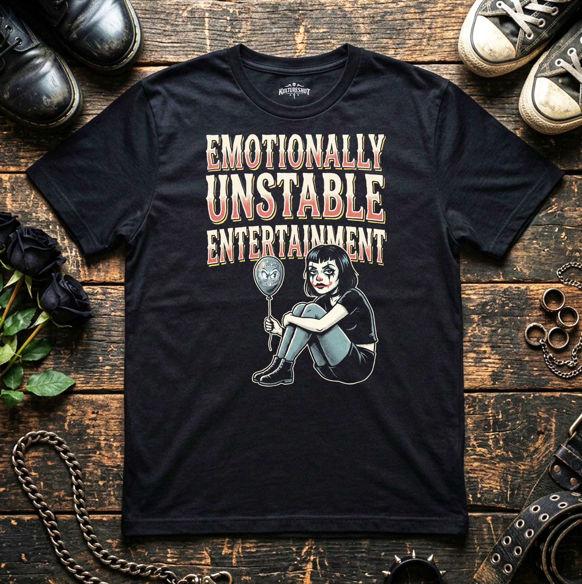 Black t-shirt with graphic design and text on a wooden surface with shoes and flowers.