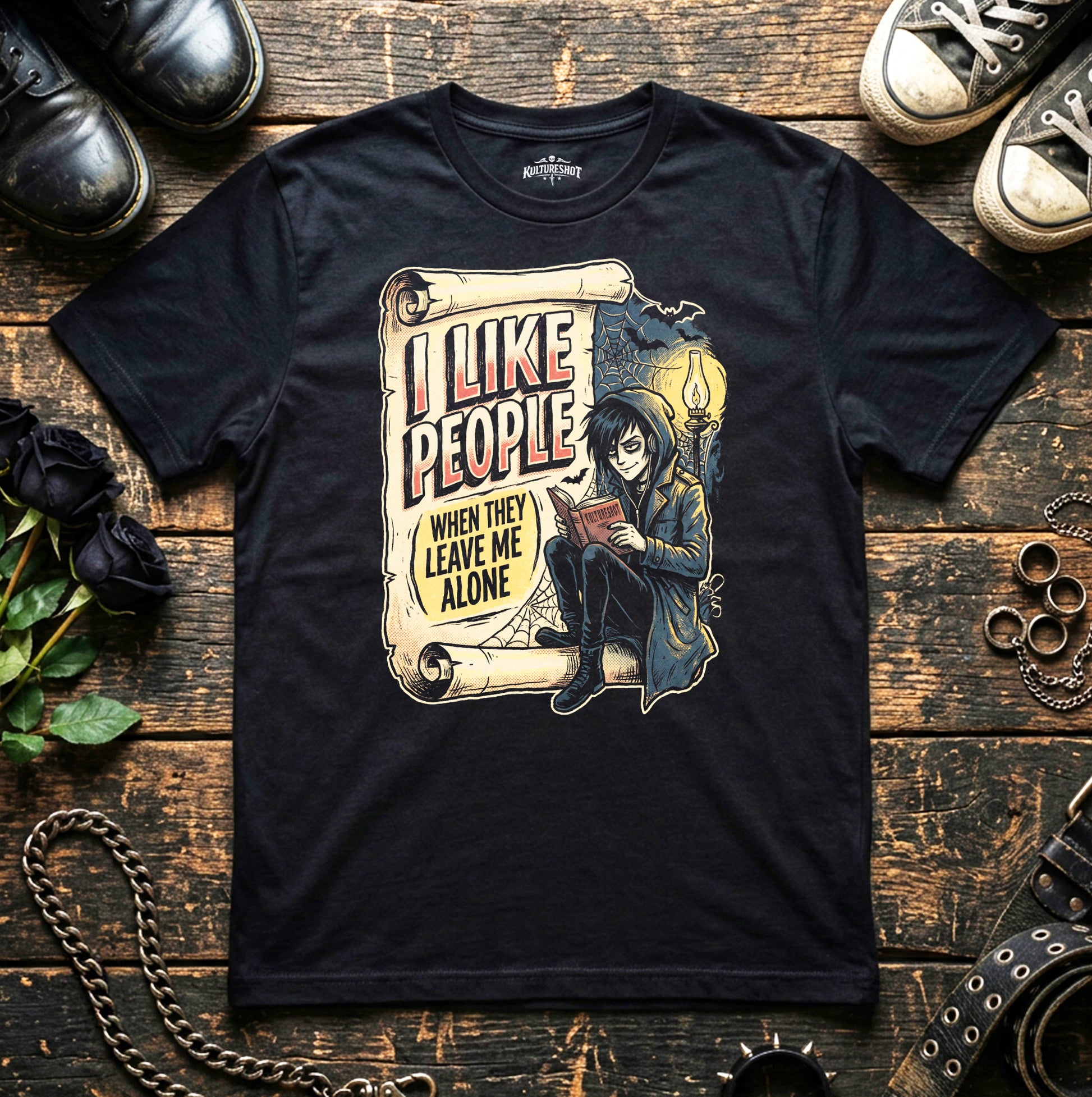 Black t-shirt with graphic design and text on a wooden surface with shoes and flowers.