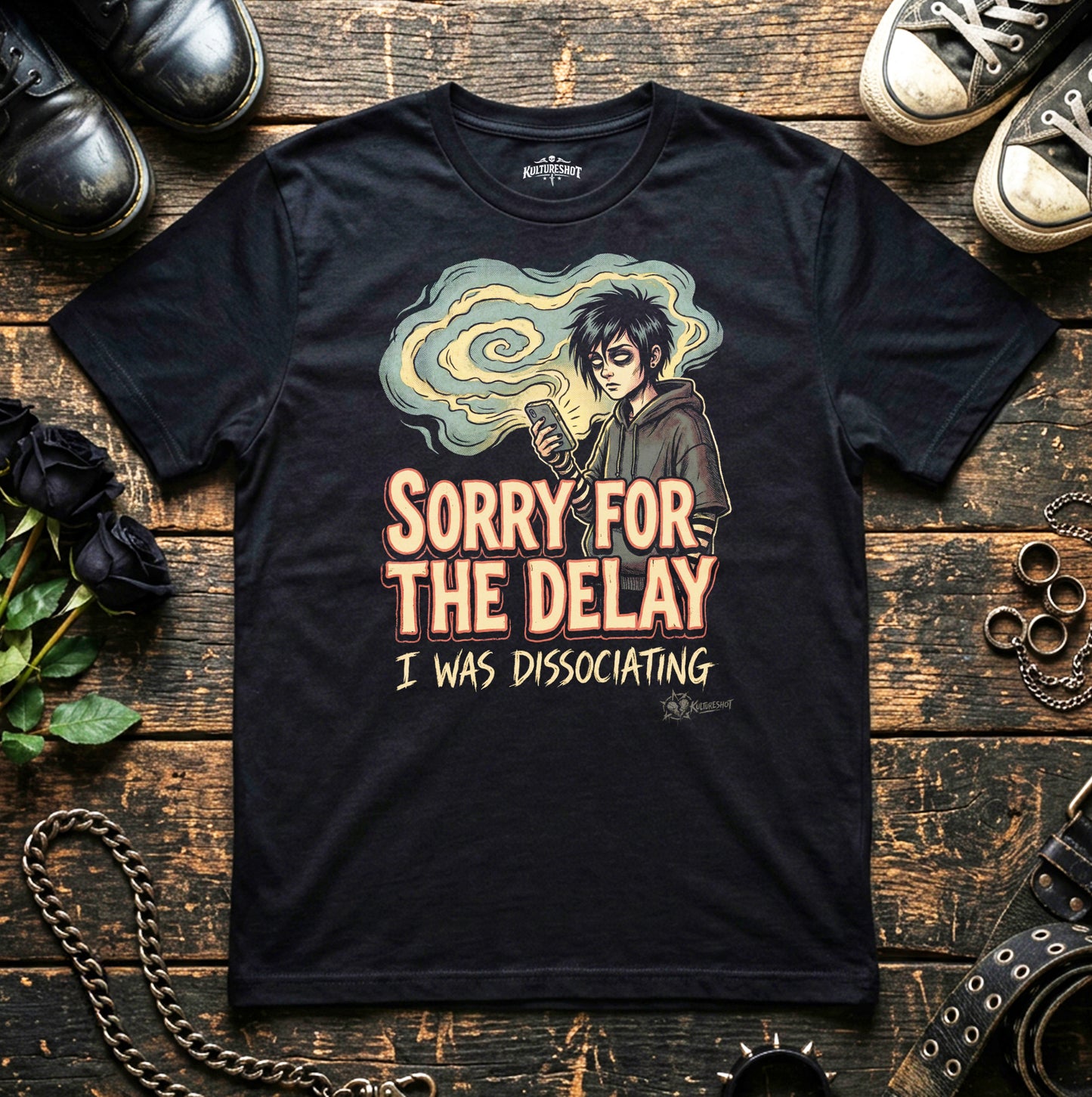 Black t-shirt with graphic design and text on a wooden surface with shoes and plants.