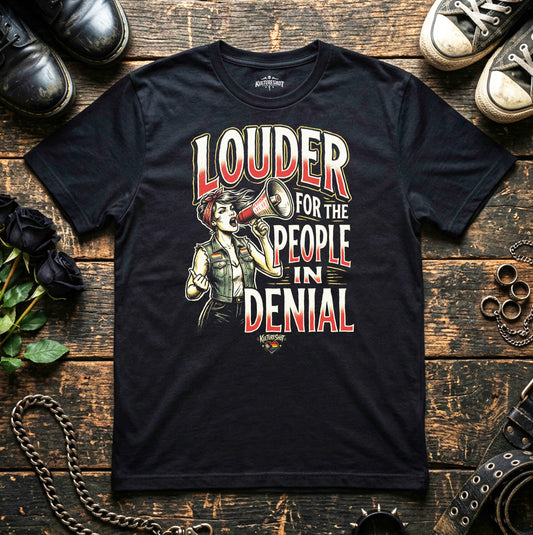 Black t-shirt with graphic design and text on a wooden surface with shoes and flowers.