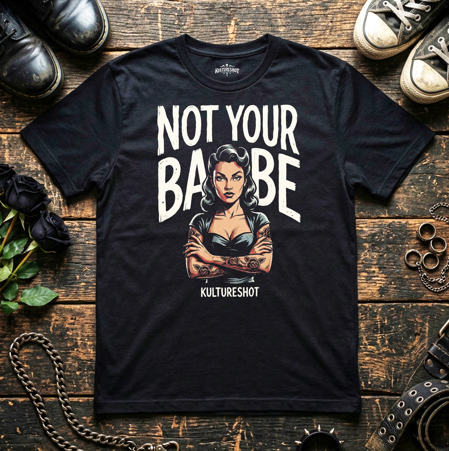 Black t-shirt with graphic design and text on a wooden surface with shoes and roses.