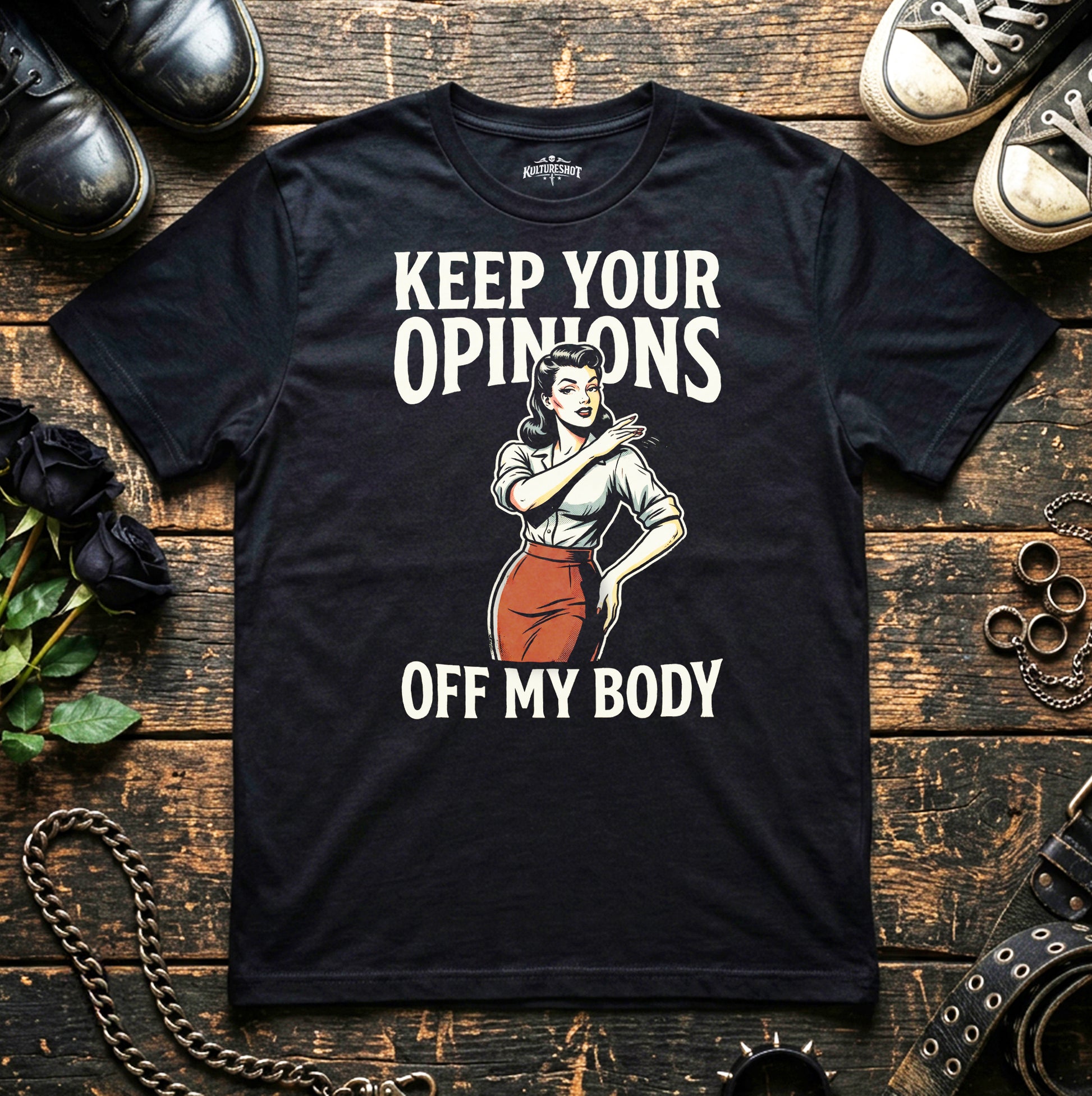 Black t-shirt with graphic and text on a wooden surface with shoes and flowers.