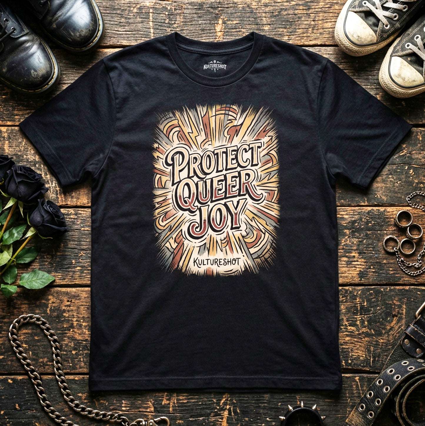 Black t-shirt with 'Protect Queer Joy' design on a wooden surface with shoes and flowers.