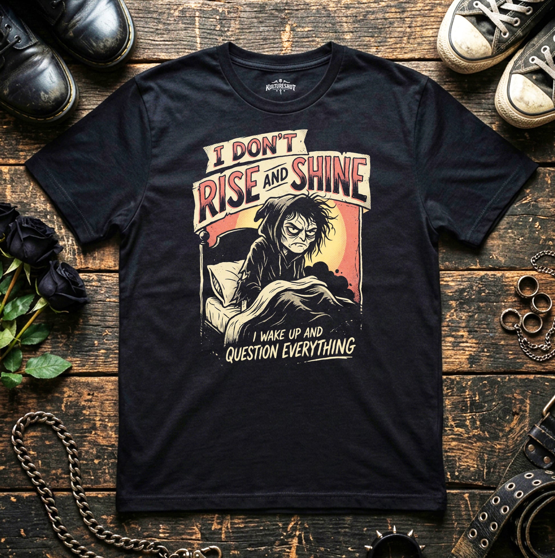 Black t-shirt with graphic design and text on a wooden surface with shoes and flowers.