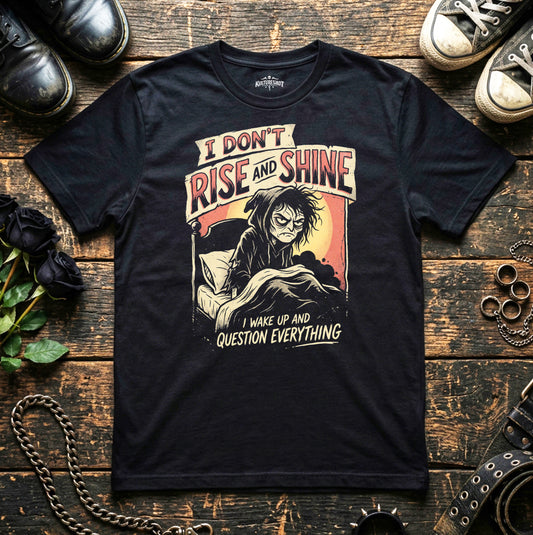 Black t-shirt with graphic design and text on a wooden surface with shoes and flowers.