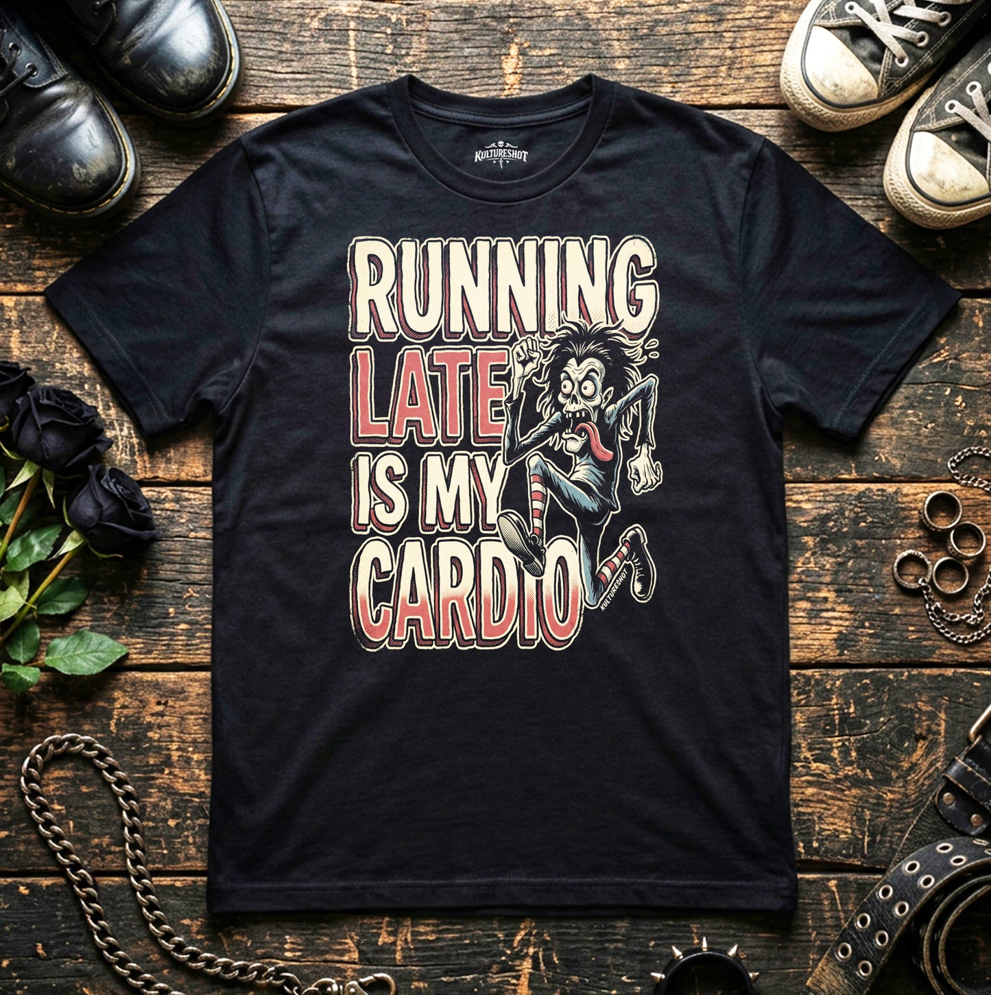 Black t-shirt with graphic design and text on a wooden surface with shoes and accessories.