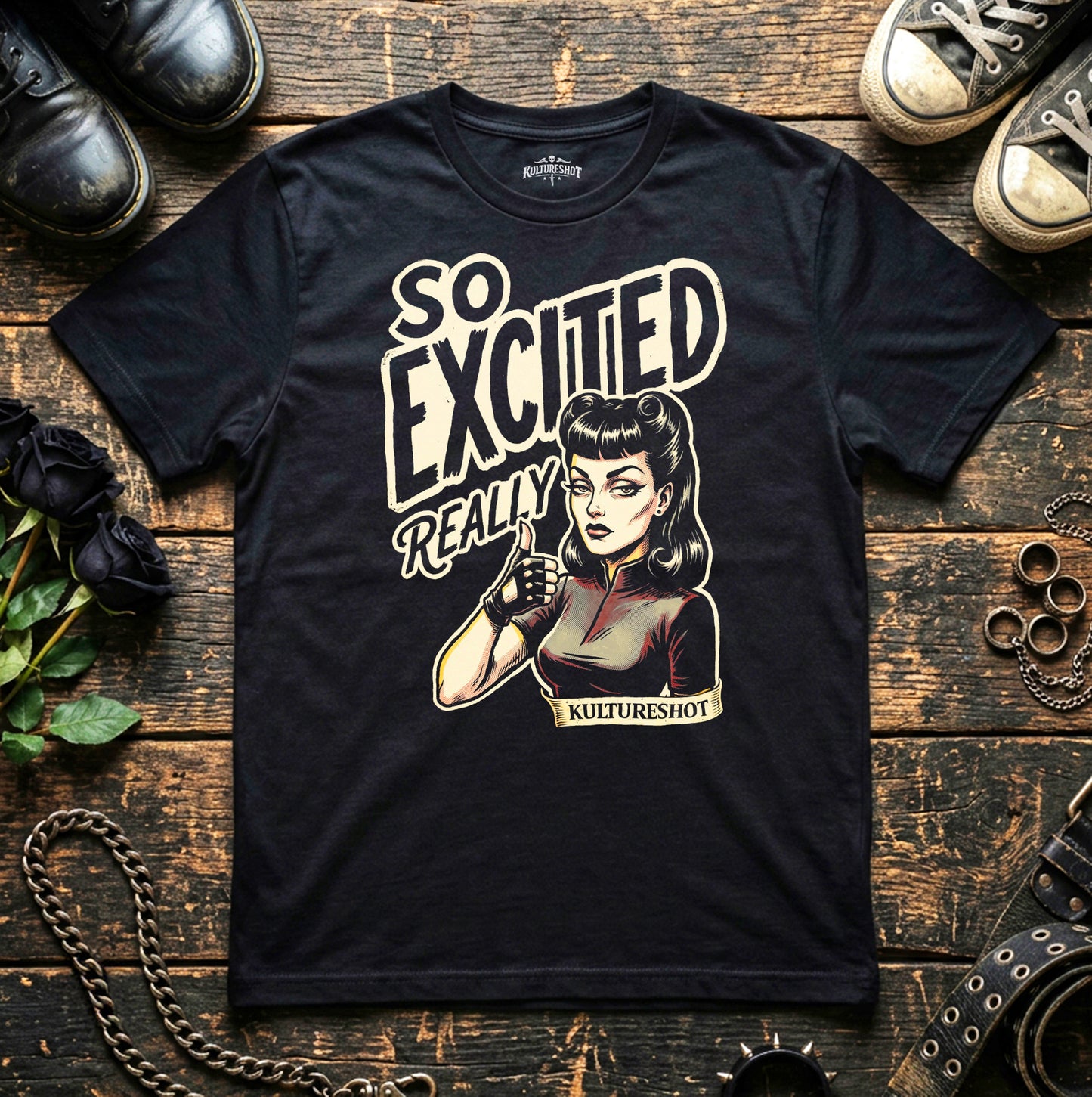 Black t-shirt with graphic design and text on a wooden surface with shoes and flowers.