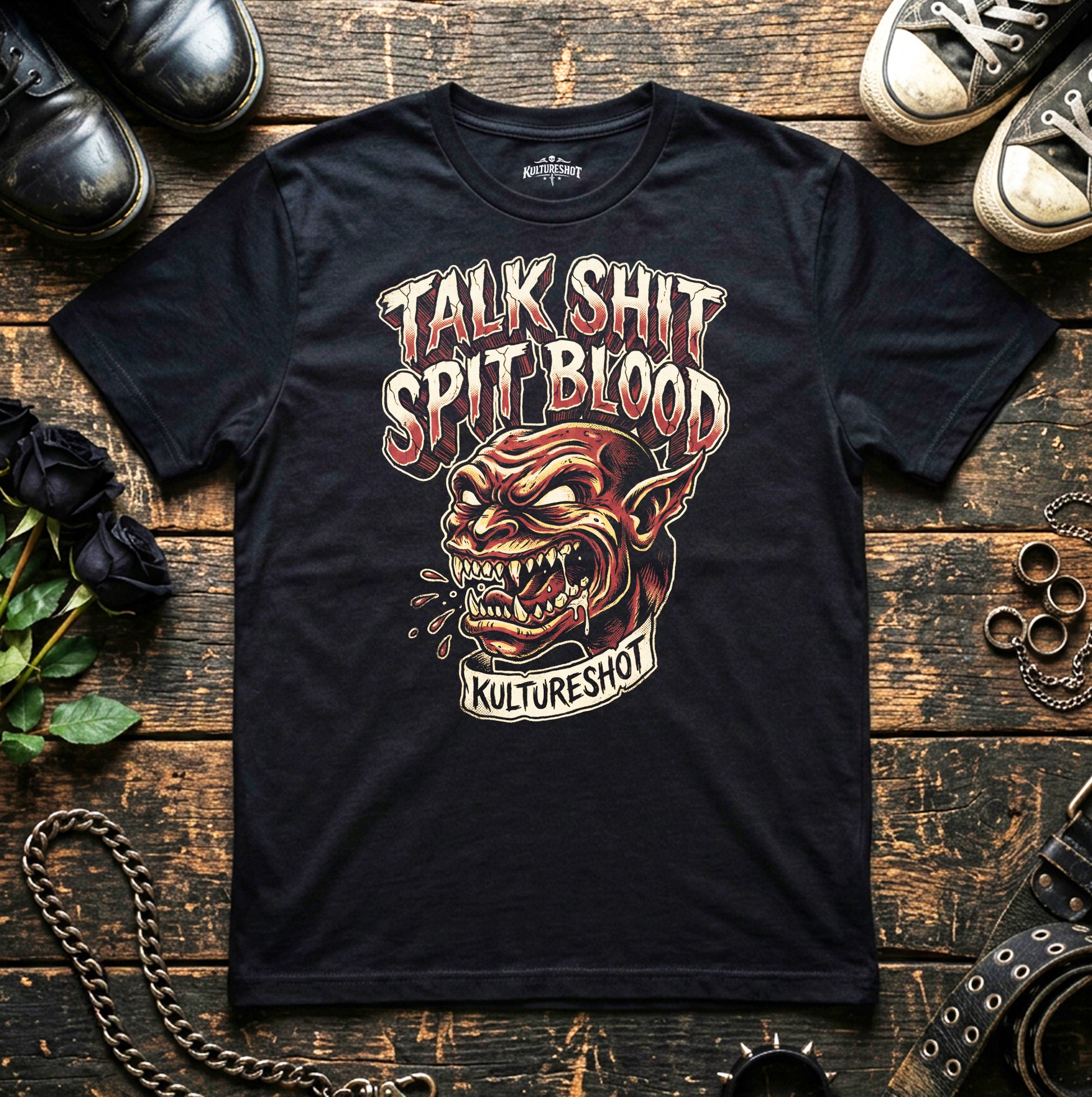 Black t-shirt with graphic design and text on a wooden surface with shoes and chains.