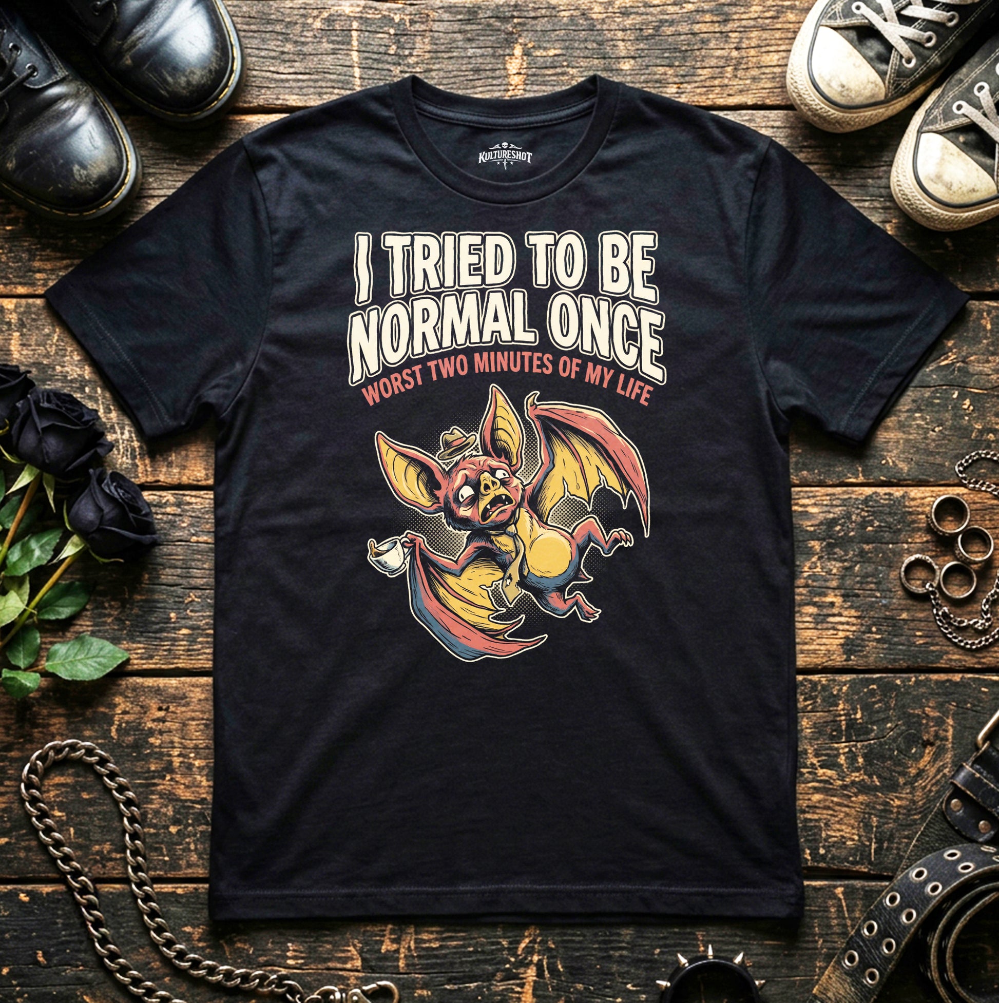 Black t-shirt with a graphic design and text on a wooden surface with shoes and a chain.
