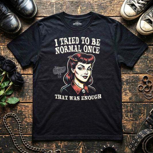 Black t-shirt with graphic design and text on a wooden surface with shoes and flowers.