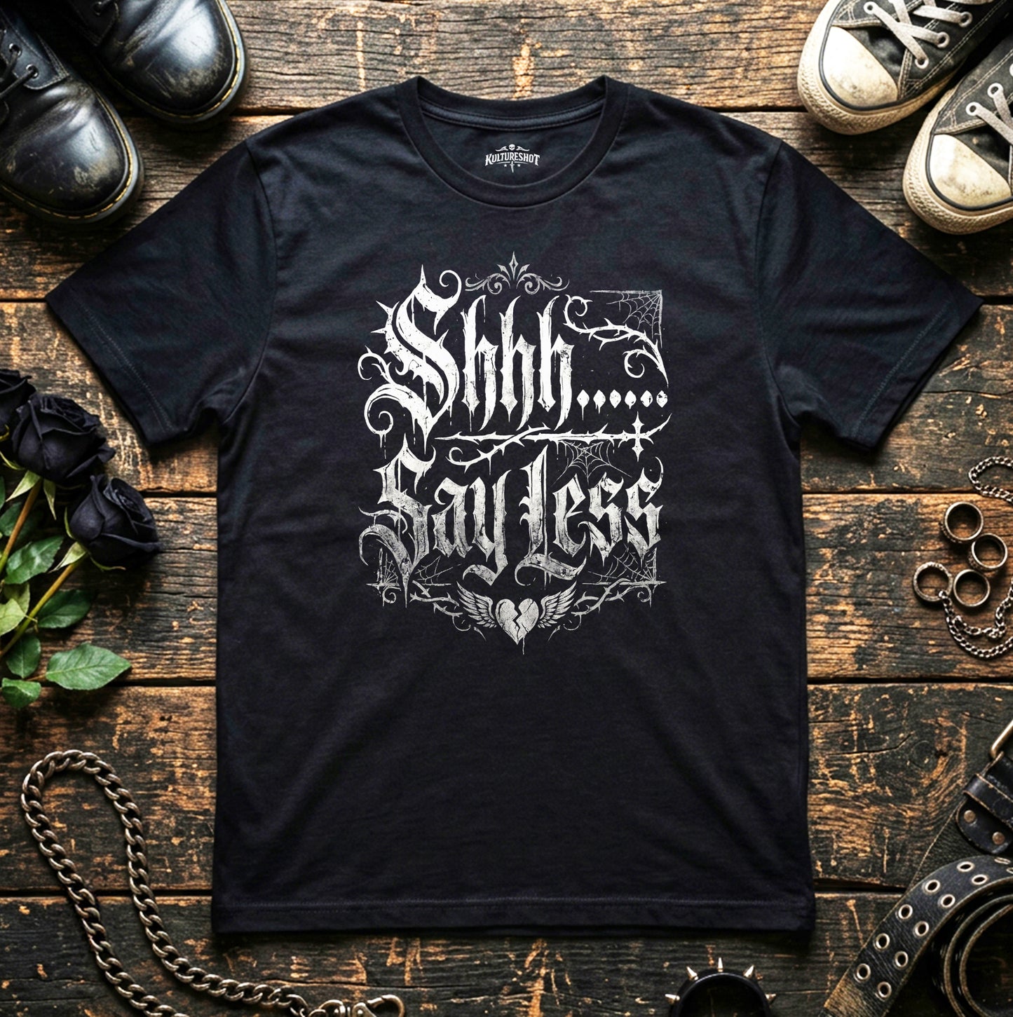 Black t-shirt with white text on a wooden surface with shoes and chains.