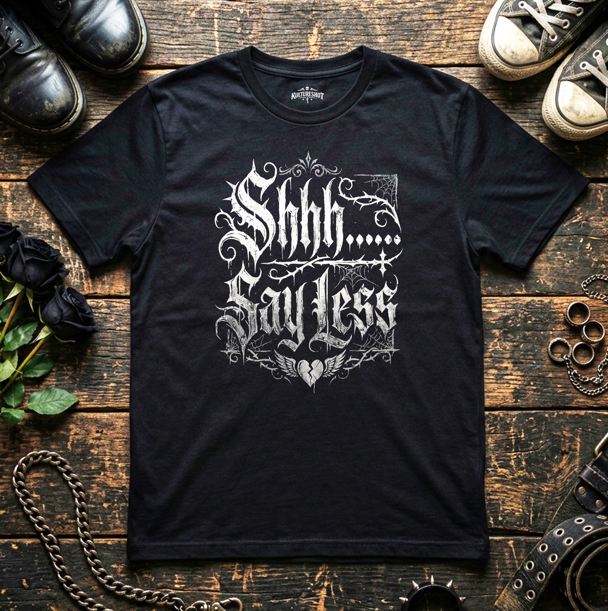 Black t-shirt with white text on a wooden surface with shoes and chains.