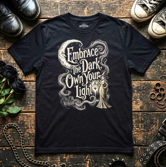 Black t-shirt with a graphic design and text on a wooden surface with shoes and roses.