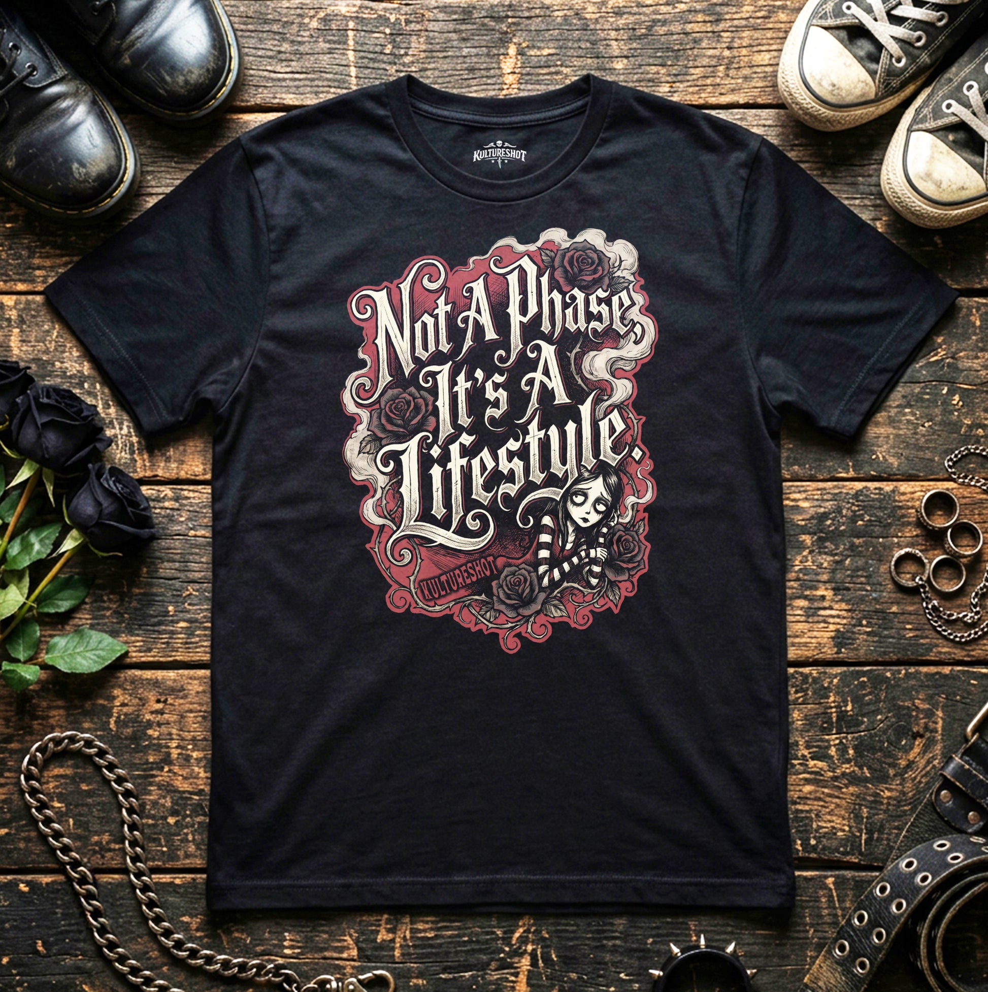 Black t-shirt with graphic design and text on a wooden surface with shoes and chains.