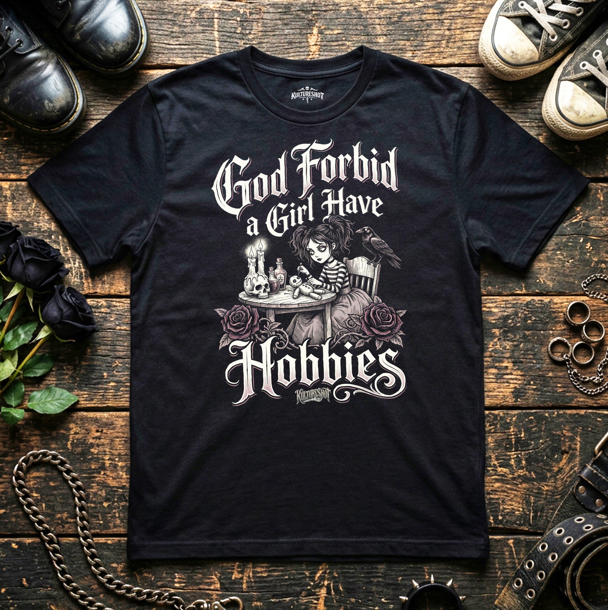 Black t-shirt with graphic design and text on a wooden surface with shoes and roses.