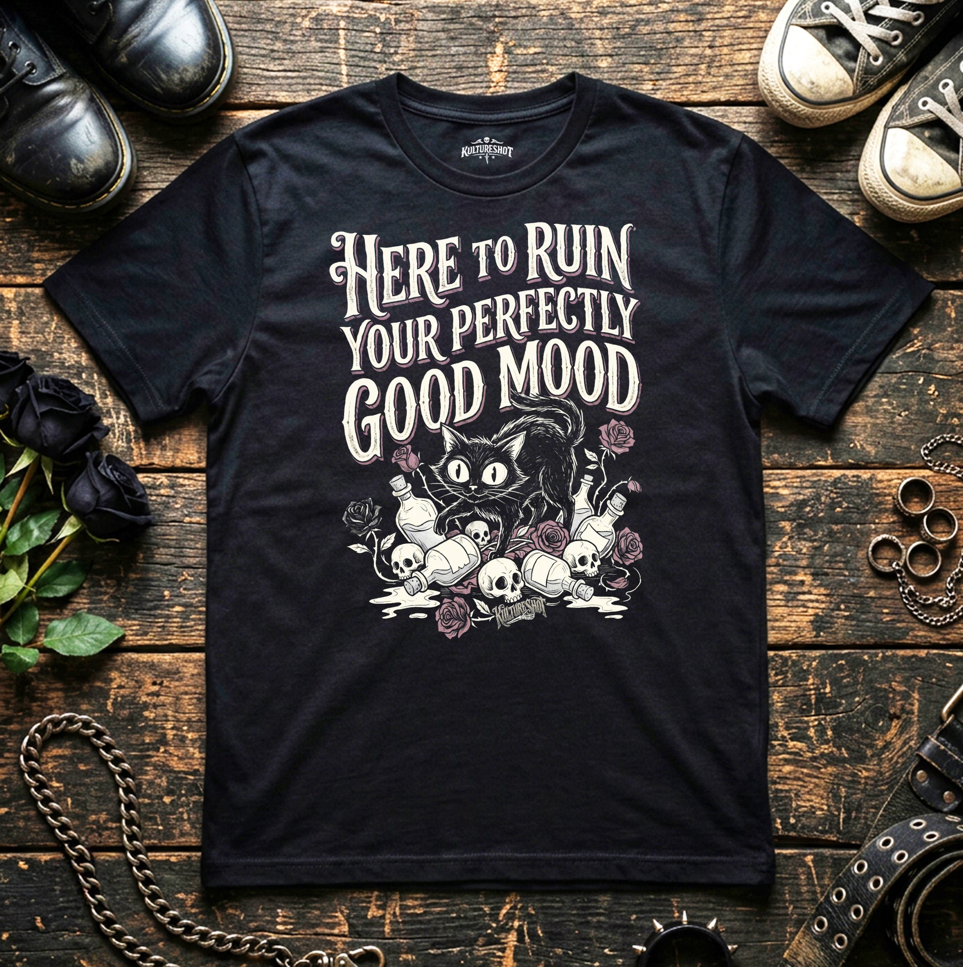 Black t-shirt with graphic design and text on a wooden surface with shoes and flowers.