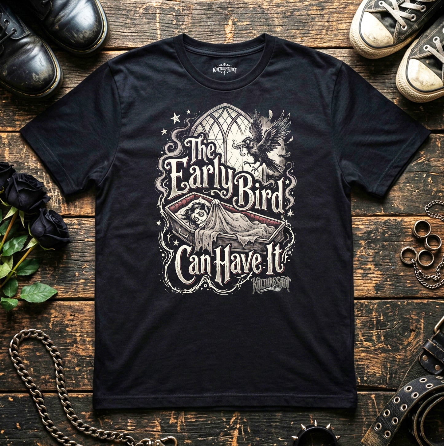 Black t-shirt with graphic design on a wooden surface with shoes and decorative items.