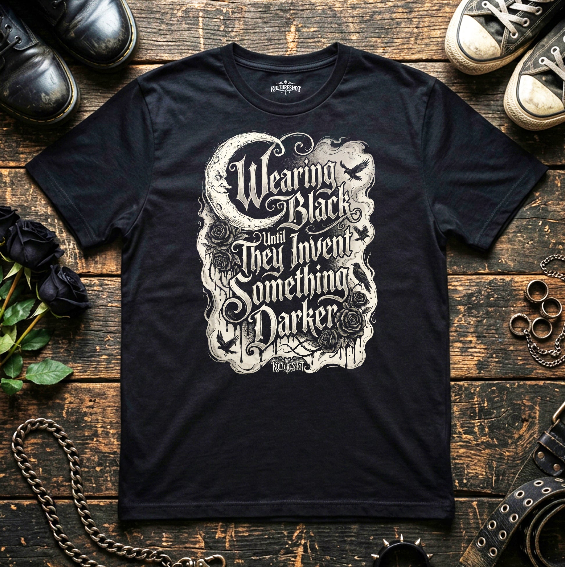 Black t-shirt with white graphic design on a wooden surface with shoes and roses.