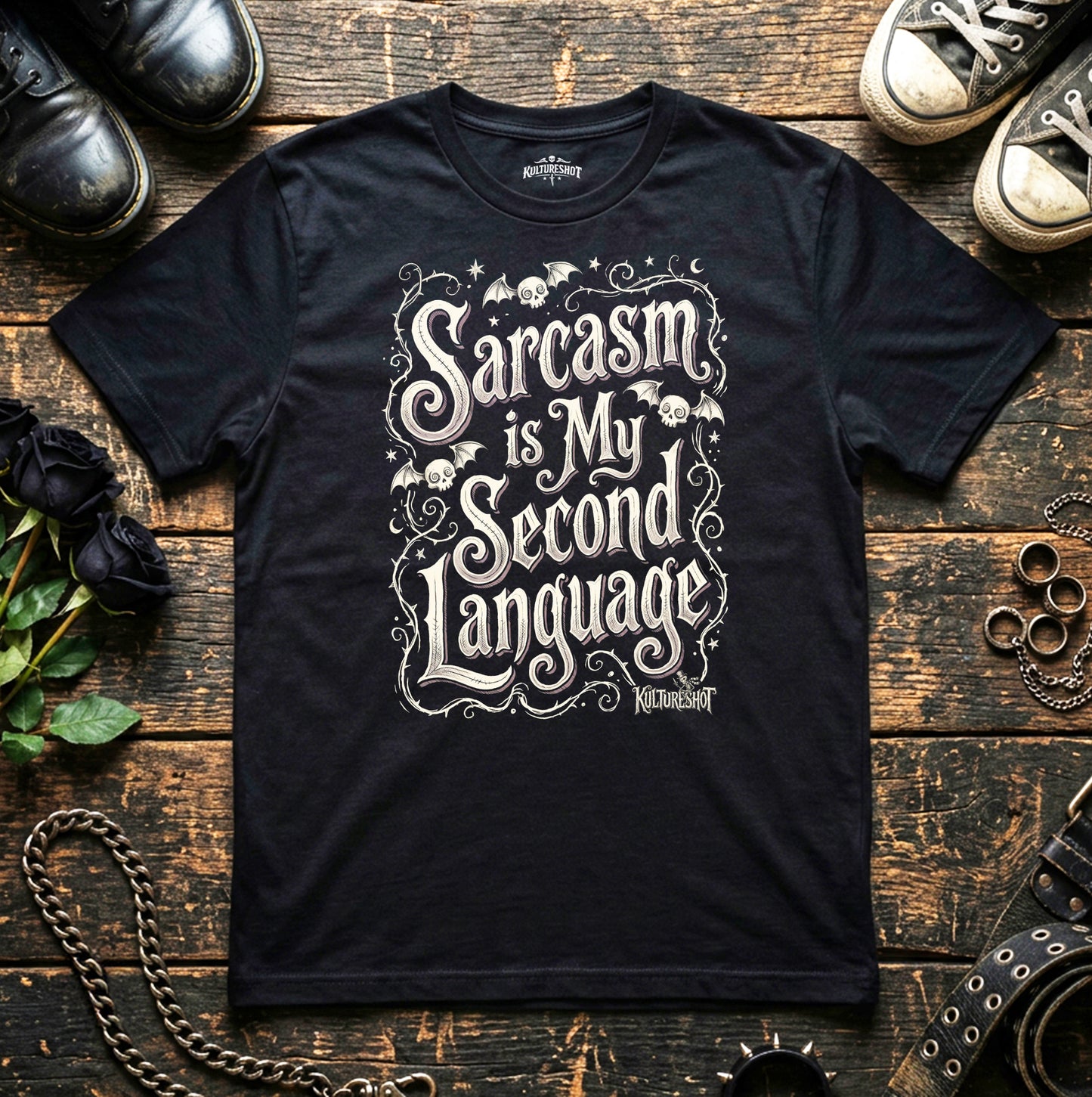 Black t-shirt with 'Sarcasm is My Second Language' text on a wooden surface with shoes and accessories.