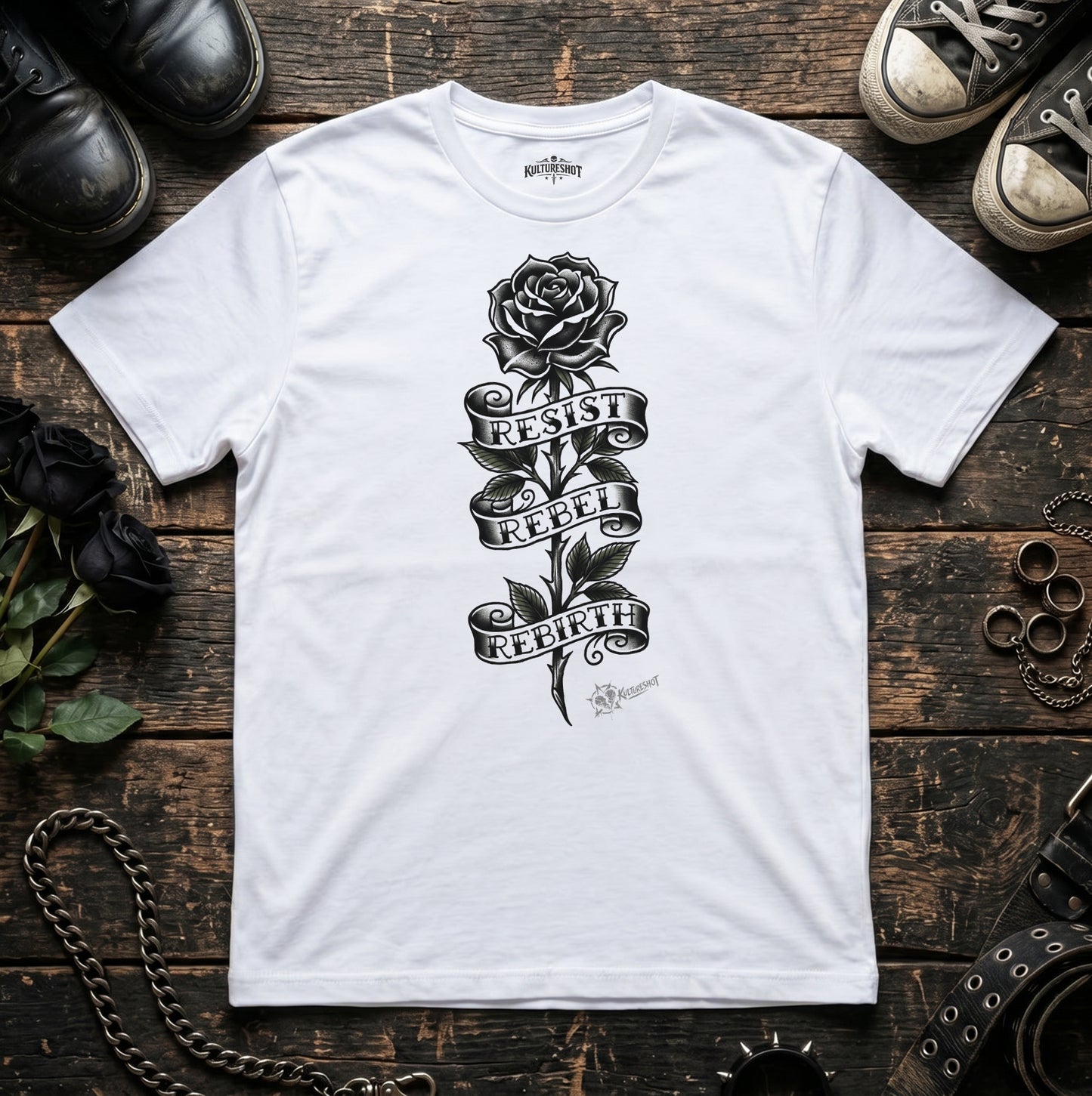 White t-shirt with black rose design and text on a wooden surface with shoes and jewelry.