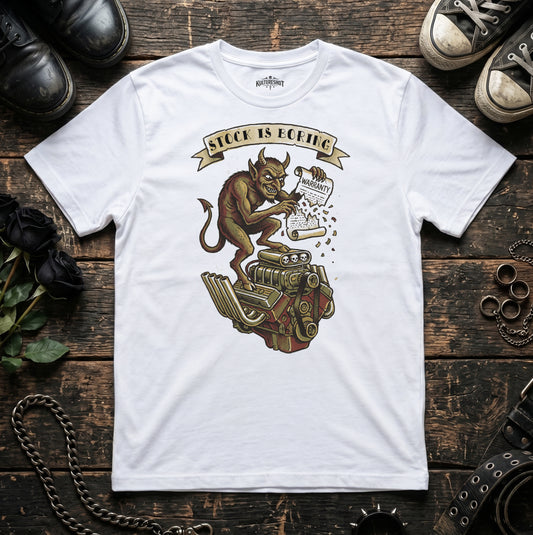 White t-shirt with a graphic design of a demon on a engine and 'Stock is Boring' text, placed on a wooden surface with shoes and a chain.