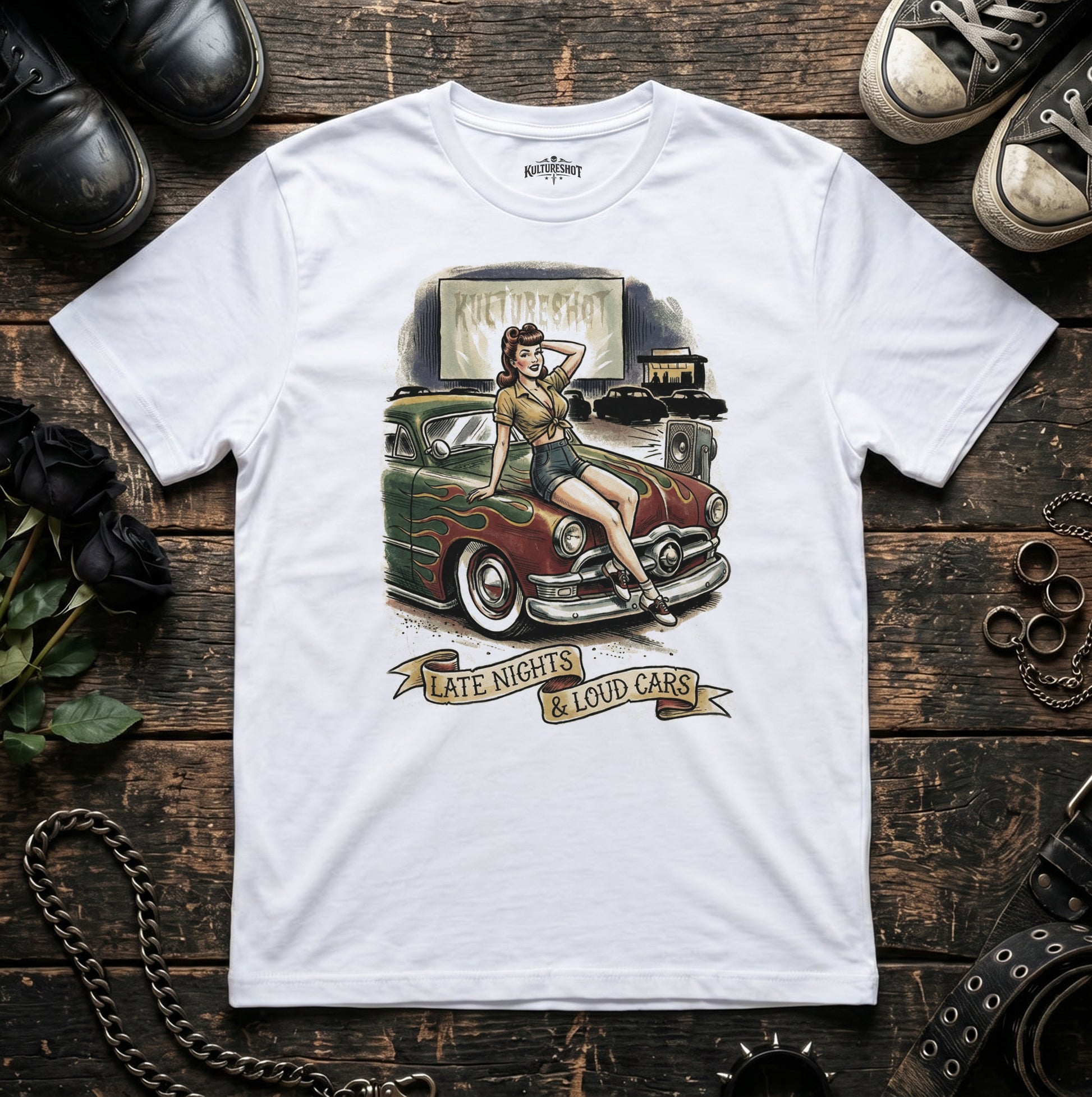 White t-shirt with a graphic of a woman by a vintage car on a wooden surface.