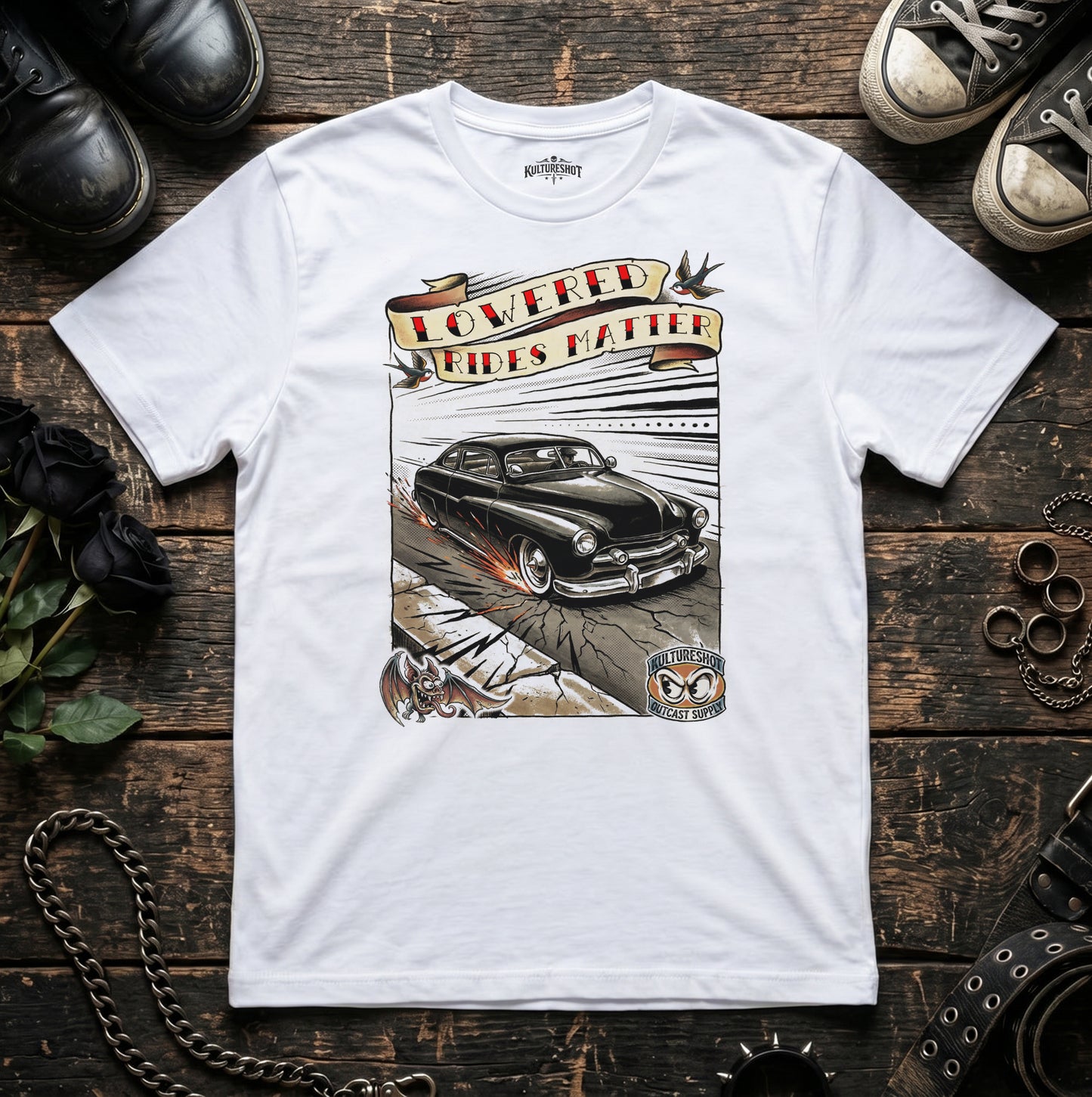 White t-shirt with a graphic of a classic car and text on a wooden surface with shoes and a chain.