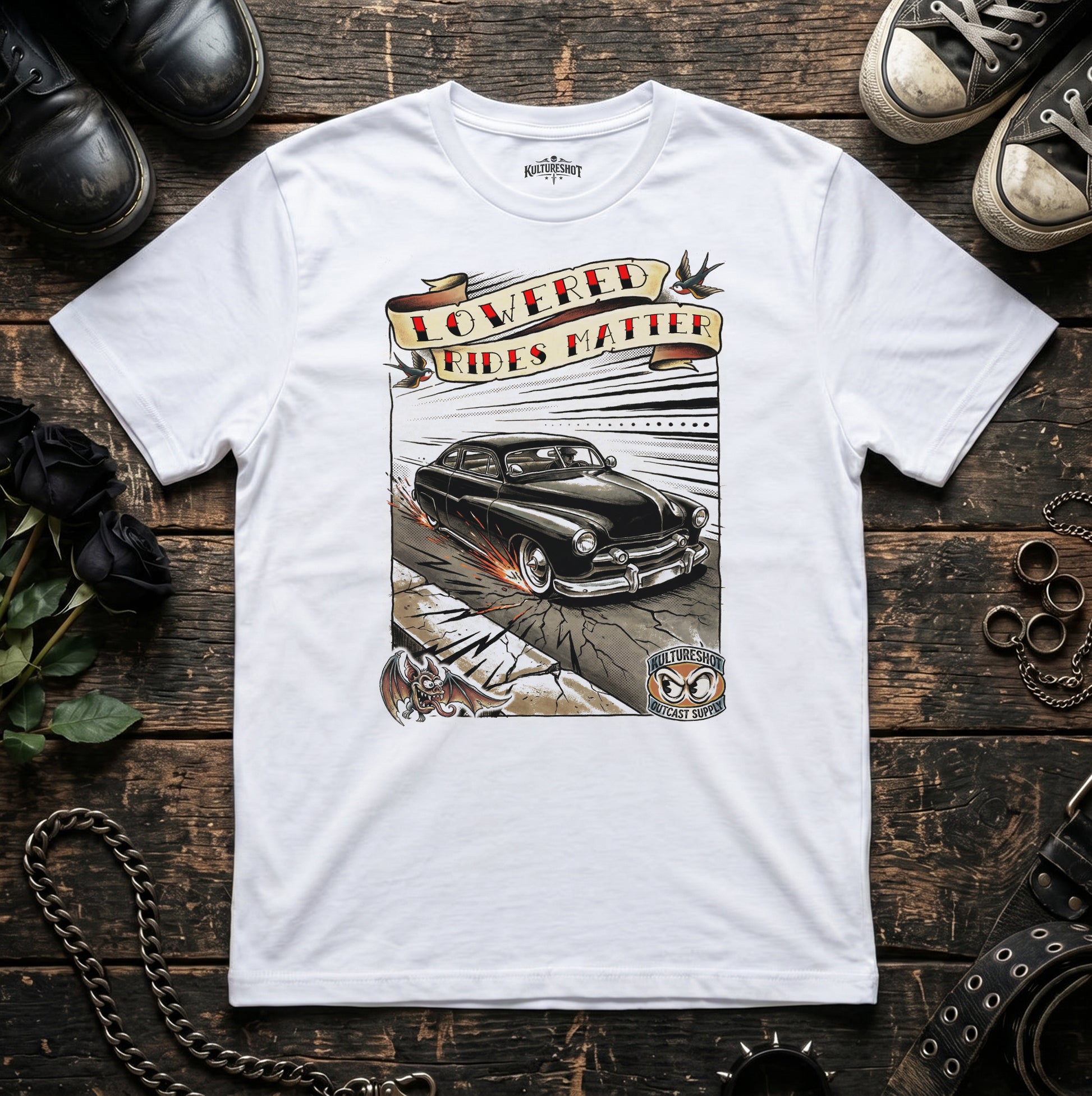 White t-shirt with a graphic of a classic car and text on a wooden surface with shoes and a chain.