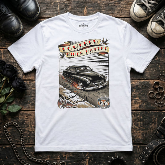 White t-shirt with a graphic of a classic car and text on a wooden surface with shoes and a chain.