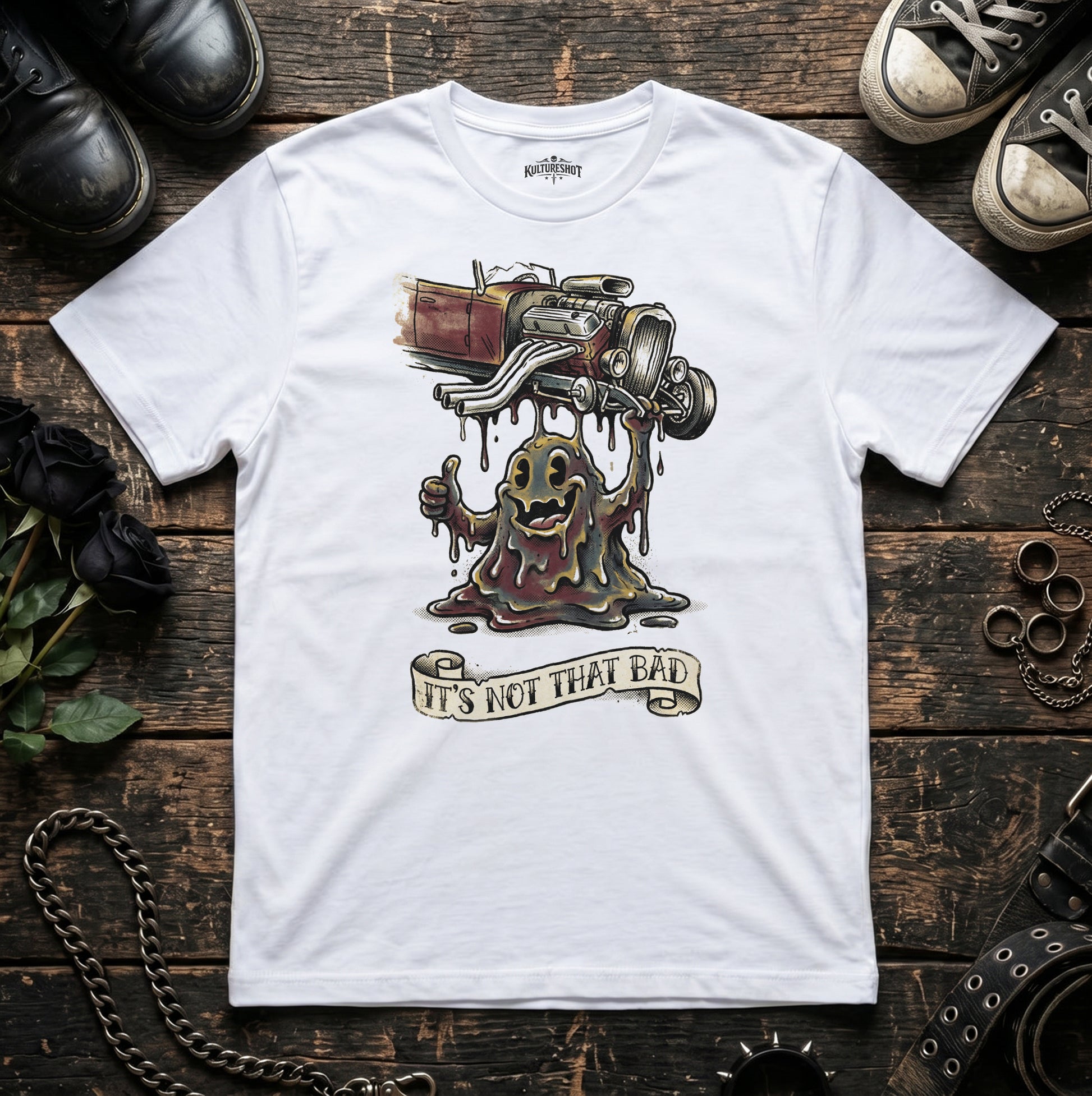 White t-shirt with a graphic design on a wooden surface with shoes and chains.