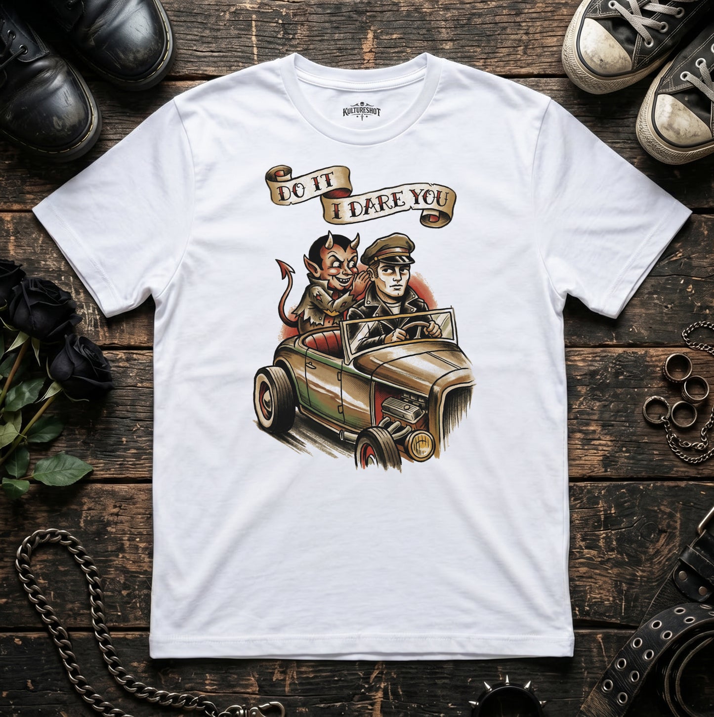 White t-shirt with a graphic design of a devil and a person in a car, with text 'Do it I dare you', on a wooden surface 