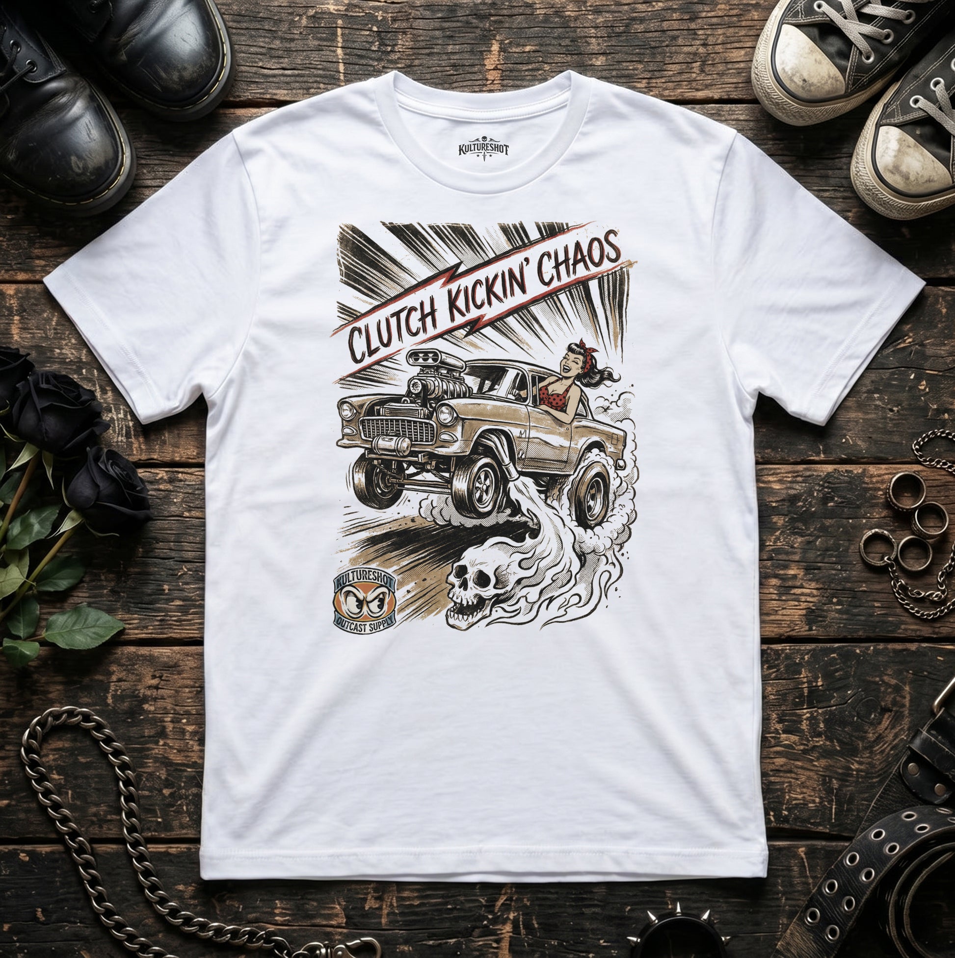 White t-shirt with a graphic design of a car and text 'Clutch Kickin' Chaos' on a wooden surface.