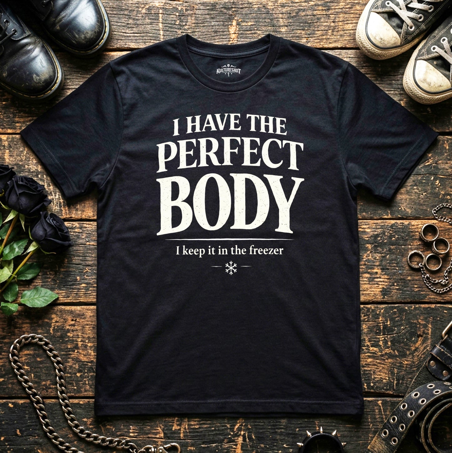 Black t-shirt with humorous text on a wooden surface with shoes and accessories.