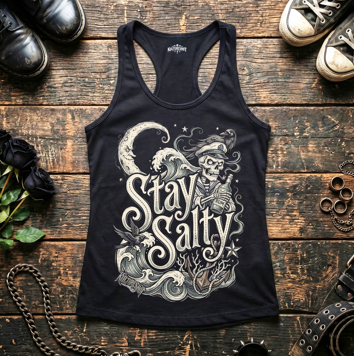 Black tank top with 'Stay Salty' graphic design on a wooden surface with shoes and accessories.
