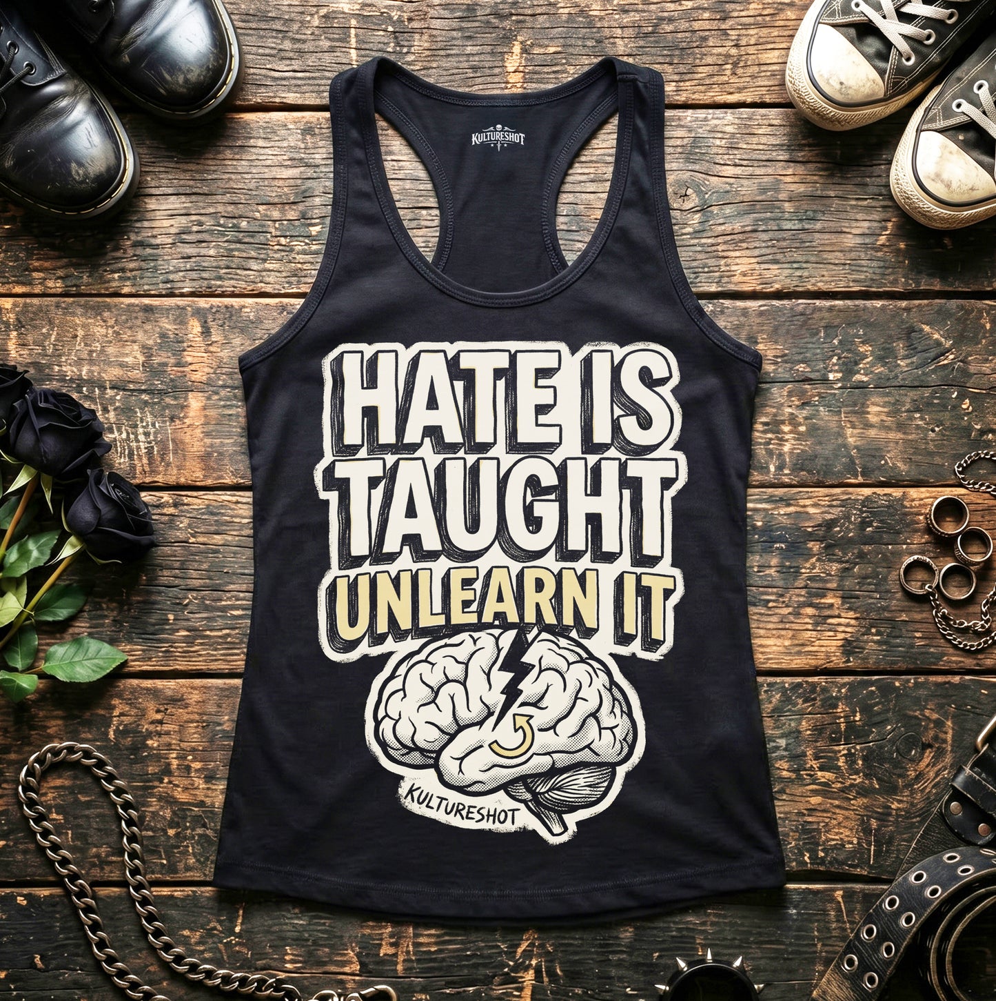 Black tank top with 'Hate is Taught, Unlearn It' text and brain graphic on a wooden surface.
