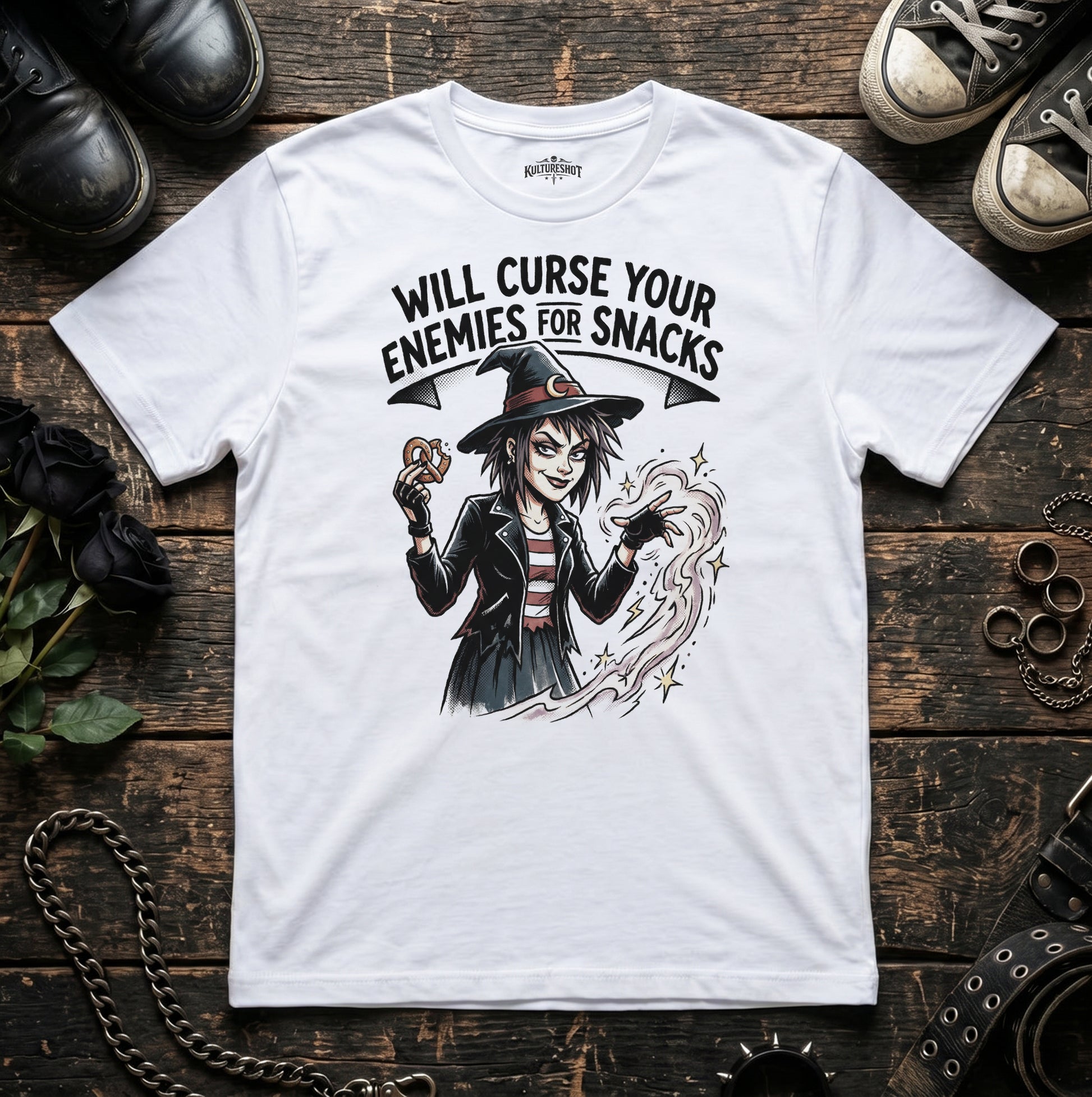 White t-shirt with a witch graphic and text on a wooden surface with shoes and jewelry.