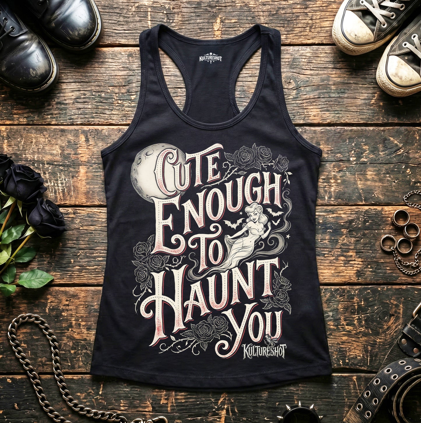 Black tank top with graphic design and text on a wooden surface with shoes and accessories.