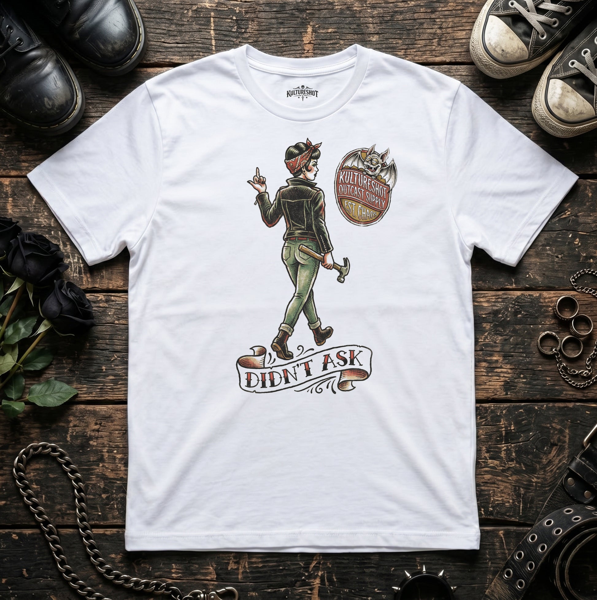 White t-shirt with graphic design on a wooden surface with shoes and accessories.