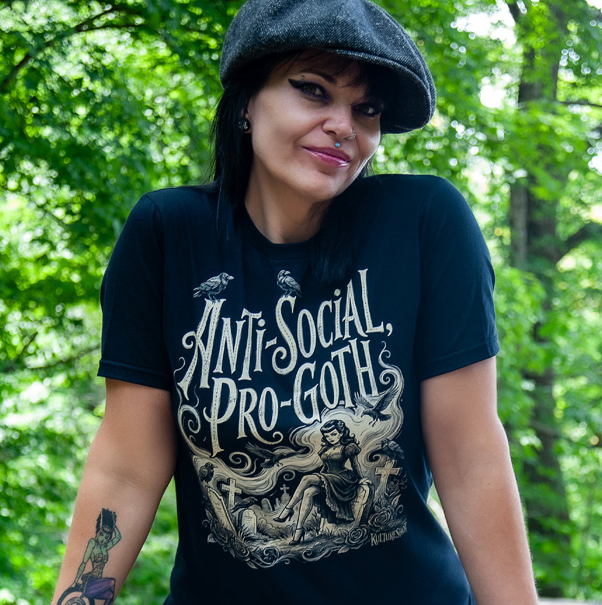 Person wearing an 'Anti-Social Pro-Goth' t-shirt sitting outdoors with greenery in the background