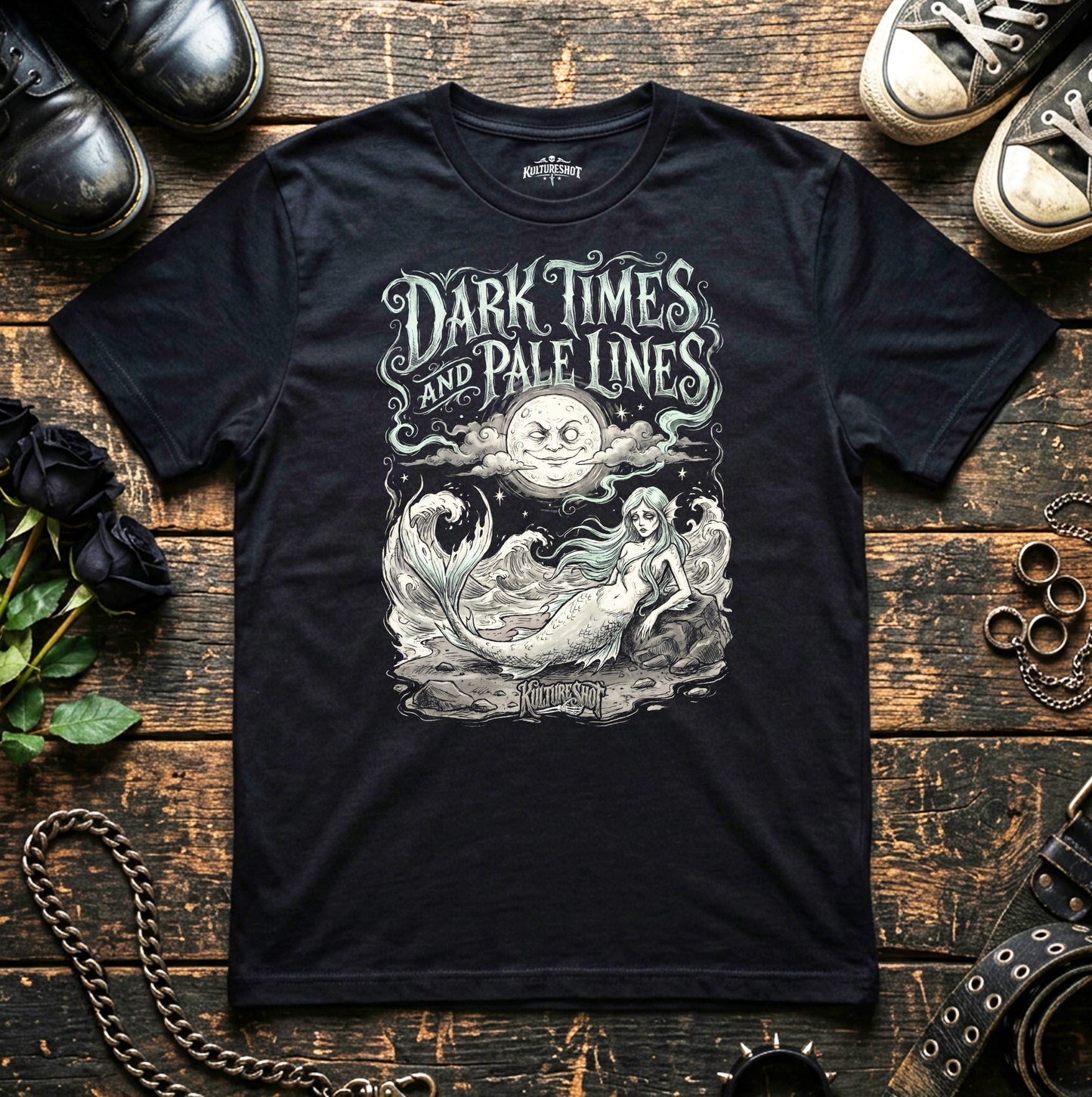 Black t-shirt with 'Dark Times and Pale Lines' design on a wooden surface with shoes and decorative items.