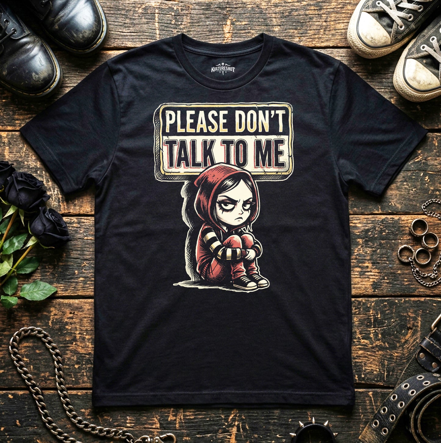 Black t-shirt with graphic reading Please Don't Talk To me, on a wooden surface with shoes and flowers.