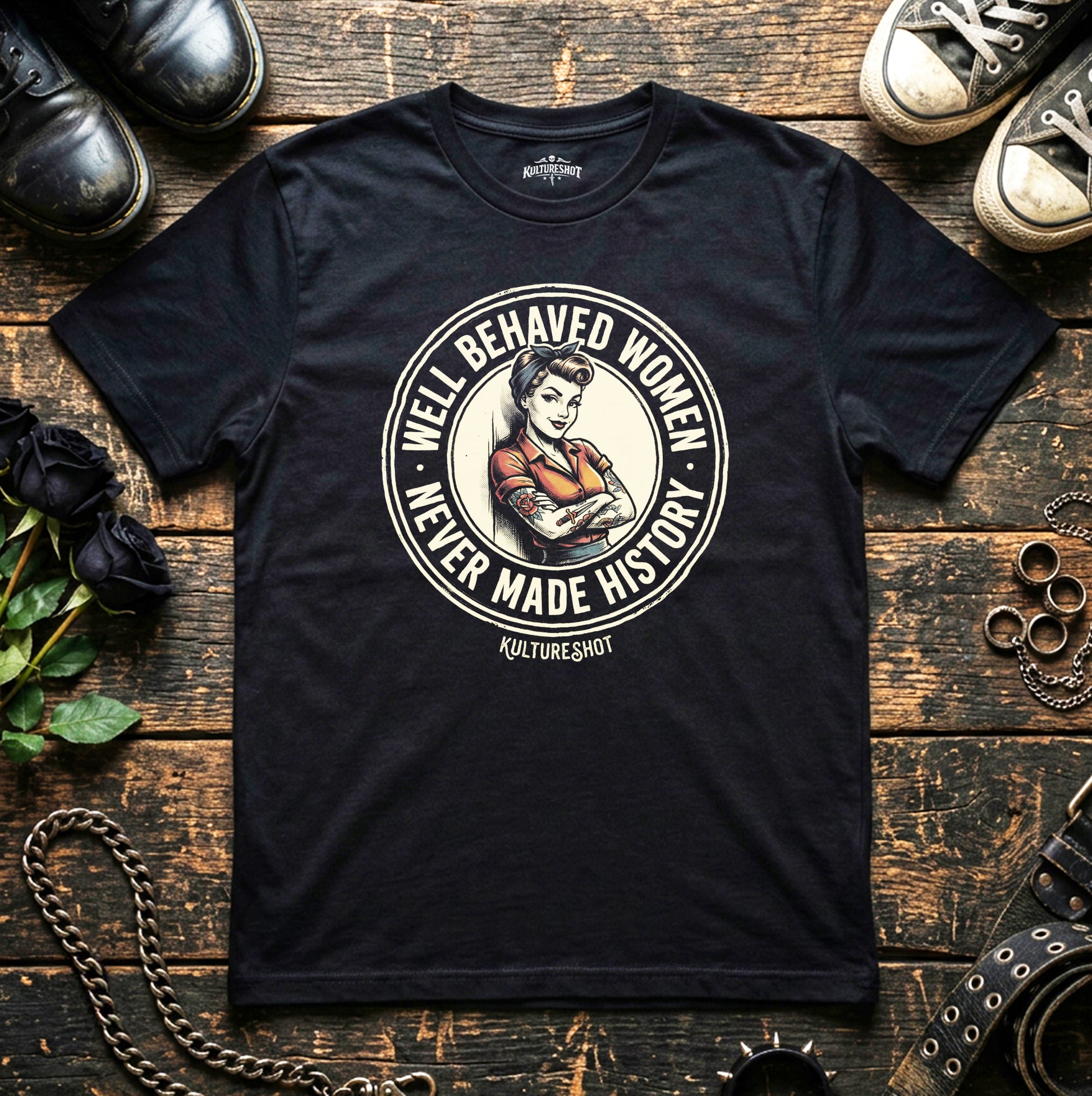 Black t-shirt with graphic design on a wooden surface with shoes and flowers.
